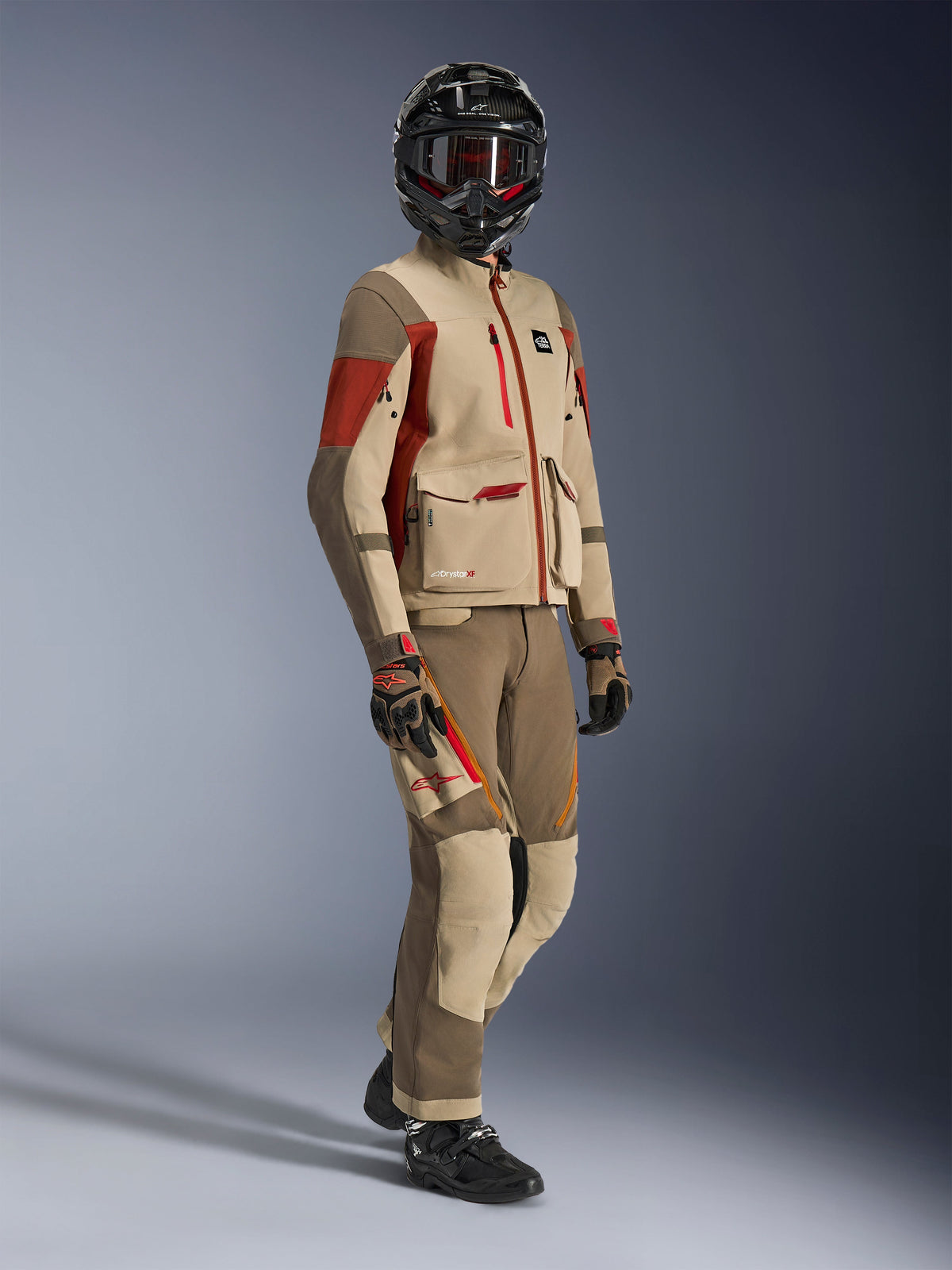 Adventure rider wearing Maxdura Drystar®XF Laminated Armored Shell, Aluminum Walnut and Rust Brown jacket with matching walnut and tan pants, black carbon fiber helmet, and black motorcycle boots, technical touring gear for adventure motorcycling