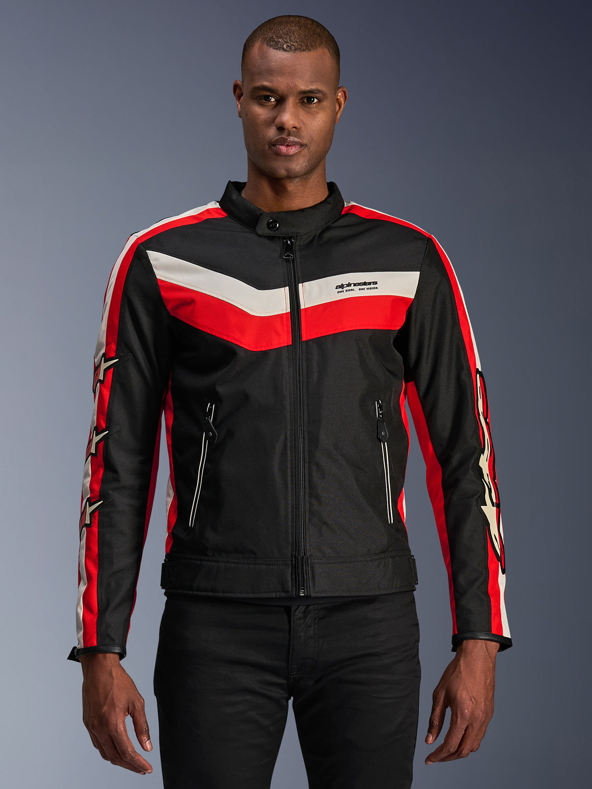 Alpinestars T-Dyno WR Jacke, Textil-Motorradjacke, Schwarz mit leuchtend roten und ecrufarbenen Chevron-Streifen, Vintage-inspirierte Biker-Passform, hoher Kragen mit Knopfverschluss, Reißverschlusstaschen vorne, Sternlogos auf den Ärmeln, von einem Model getragen