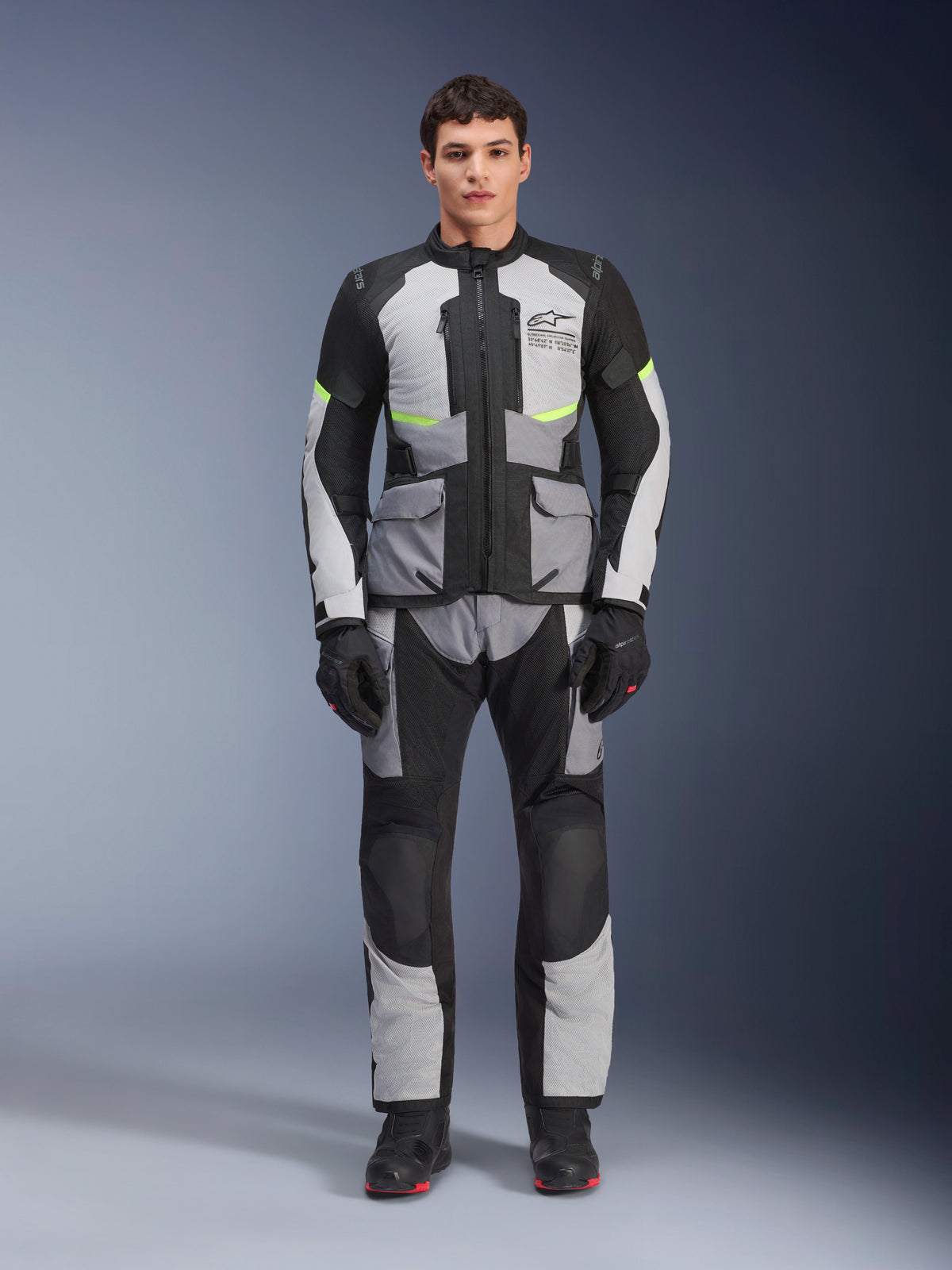 Alpinestars Andes Air Drystar® Jacke in Eisgrau, Dunkelgrau und Schwarz, getragen von einem männlichen Model mit passender Motorradhose und Handschuhen, Adventure-Touring-Design mit großen Fronttaschen und neongelben Akzenten, Studio-Frontansicht