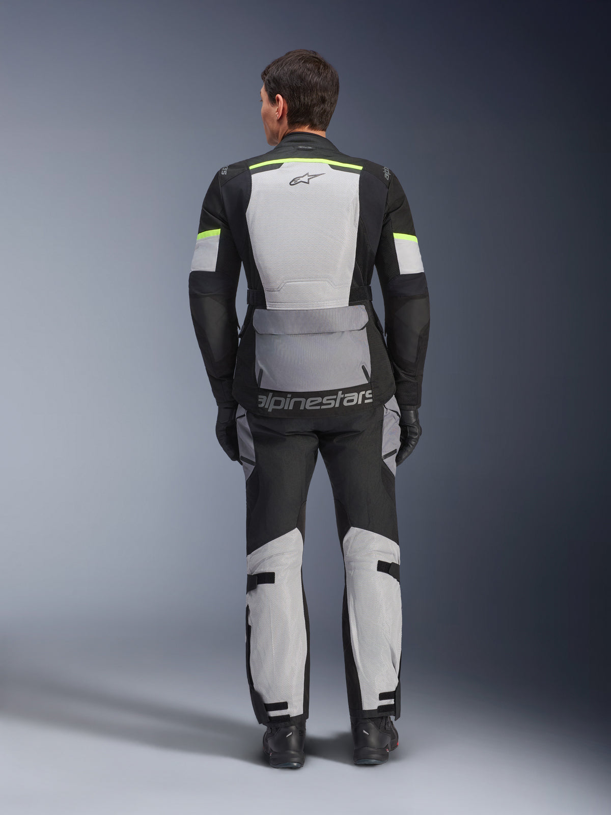 Alpinestars Andes Air Drystar® Jacke und Hose, Adventure-Touren-Set in Ice Gray, Dark Gray und Black, Rückansicht eines Fahrers in kompletter Ausrüstung mit neongelben Akzenten, große Mesh-Belüftungseinsätze und Alpinestars-Branding