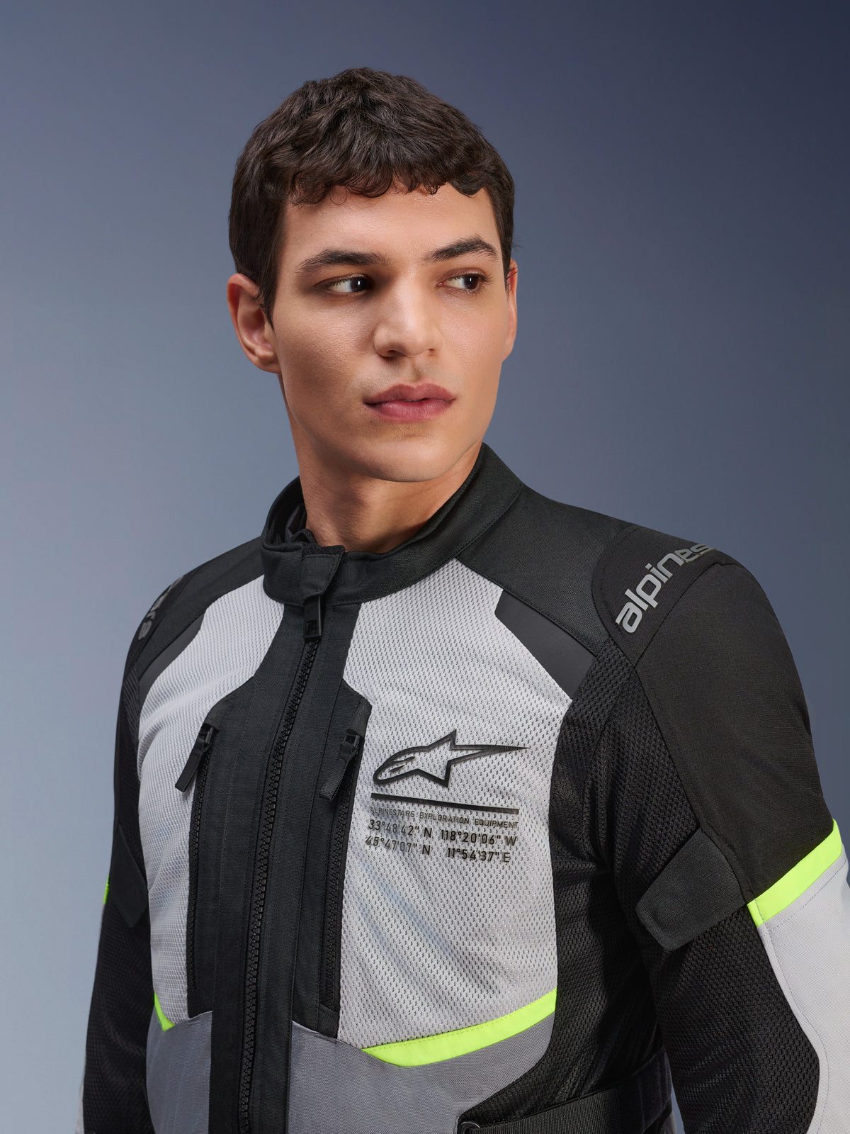 Alpinestars Andes Air Drystar® Jacke, Motorrad-Tourenjacke, Eisgrau und Dunkelgrau mit neongelben Akzenten, getragen von einem männlichen Model, 2D-Mesh-Einsätze zur Belüftung, Alpinestars-Logo mit Koordinaten auf der Brust, strapazierfähige Textilkonstruktion