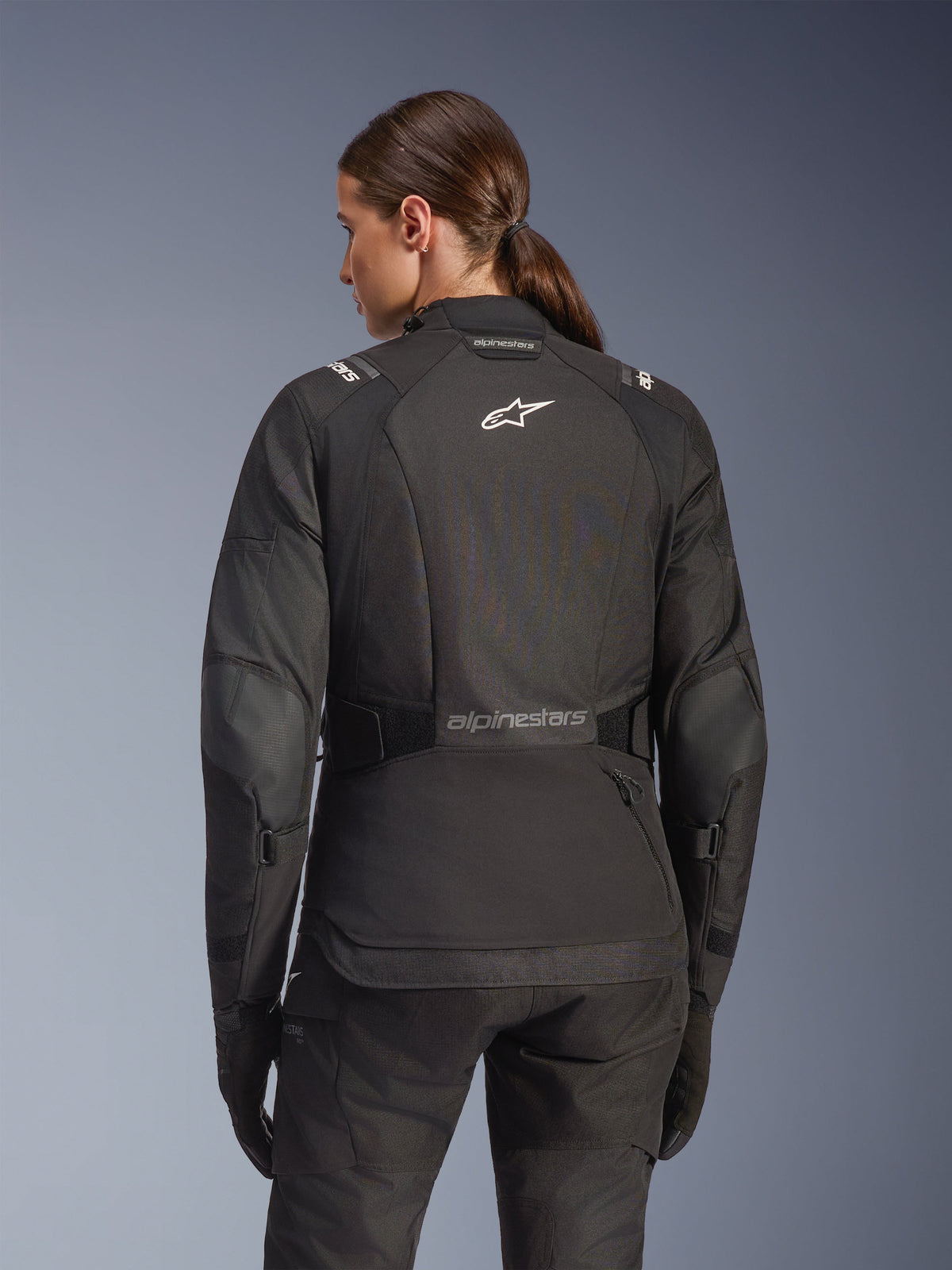 Alpinestars Stella Andes V4 Drystar Jacke für Damen in Schwarz, Rückansicht mit weißem Logo auf dem Rücken und verstärkten Ellbogenpaneelen, kombiniert mit passender schwarzer Hose und Handschuhen, Adventure-Touring-Motorradausrüstung