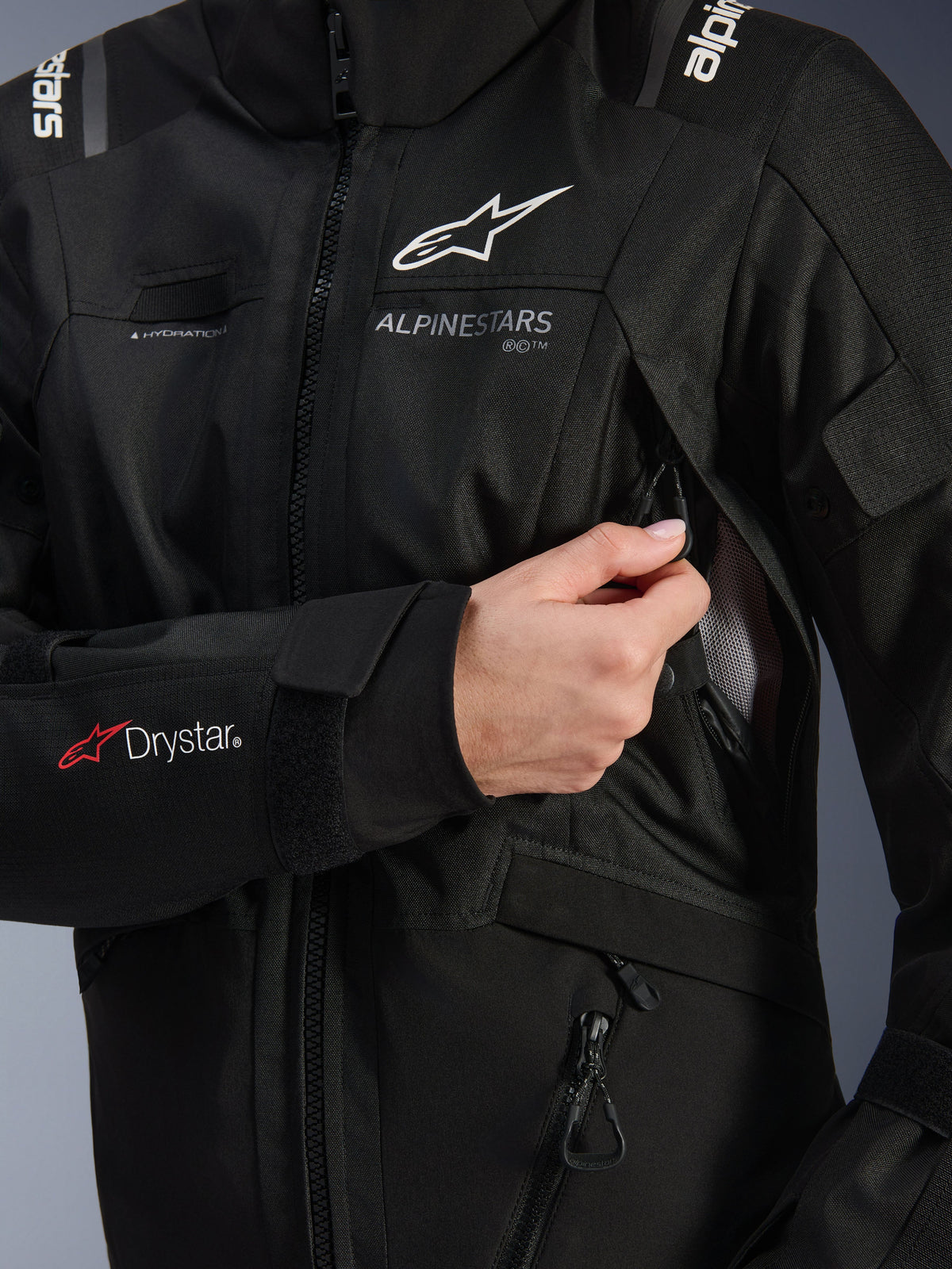 Alpinestars Damen Stella Andes V4 Drystar® Jacke, Schwarz, Detailaufnahme der geöffneten Belüftungsöffnung an der Brust, zeigt Mesh-Futter, Drystar®-Logo am Unterarm und Schlaufe für den Trinkschlauch, technische Motorradbekleidung