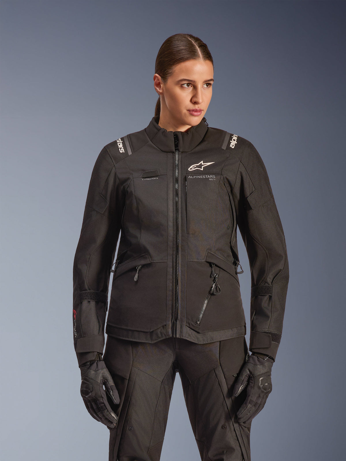 Alpinestars Stella Andes V4 Drystar Jacke, Damen-Motorrad-Tourenjacke, Schwarz, getragen von einem Modell mit passender Hose und Handschuhen, mit Reißverschluss vorne, weißem Logo auf der Brust und Alpinestars-Branding auf den Schultern, elegante Allwetterausrüstung.