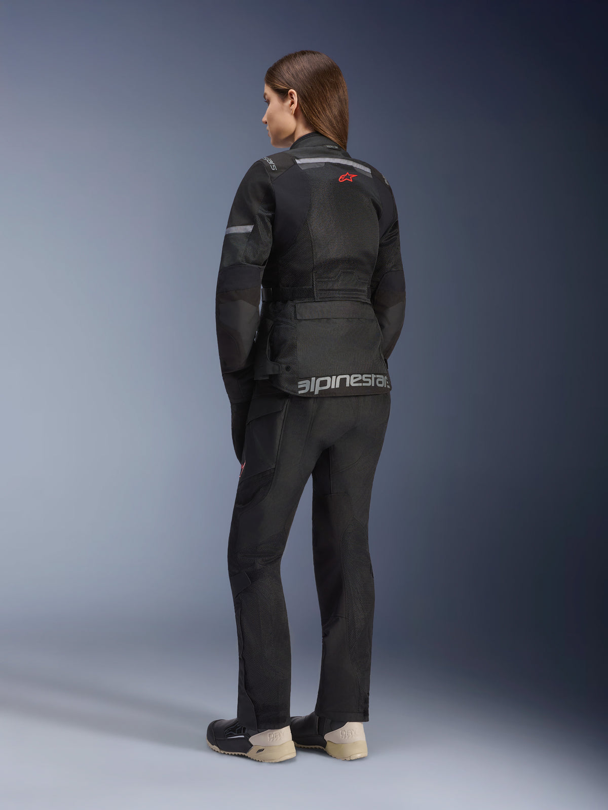 Alpinestars Stella Andes Air Drystar® Jacke, Damen-Motorrad-Tourenjacke, Schwarz, Rückansicht getragen mit passender Motorradhose und Stiefeln, mit großen Mesh-Belüftungseinsätzen, einem roten Stern-Logo und silbernem Alpinestars-Schriftzug am unteren Rücken.