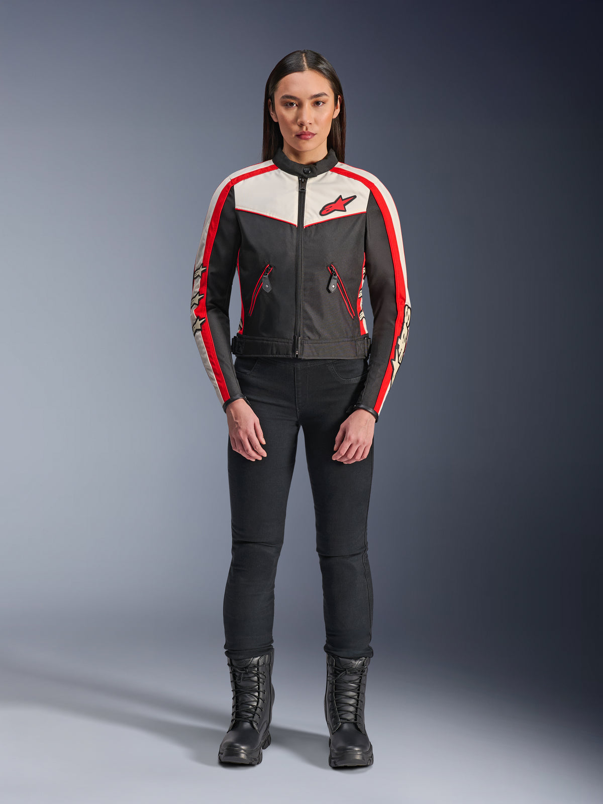Alpinestars Stella T-Dyno WR Jacke, Textil-Motorradjacke für Damen, Schwarz, Ecru und Bright Red, getragen von einem Model mit schwarzer Hose und Stiefeln, mit Vintage-inspiriertem Design, rotem Alpinestars-Logo und Kontrasteinsätzen.