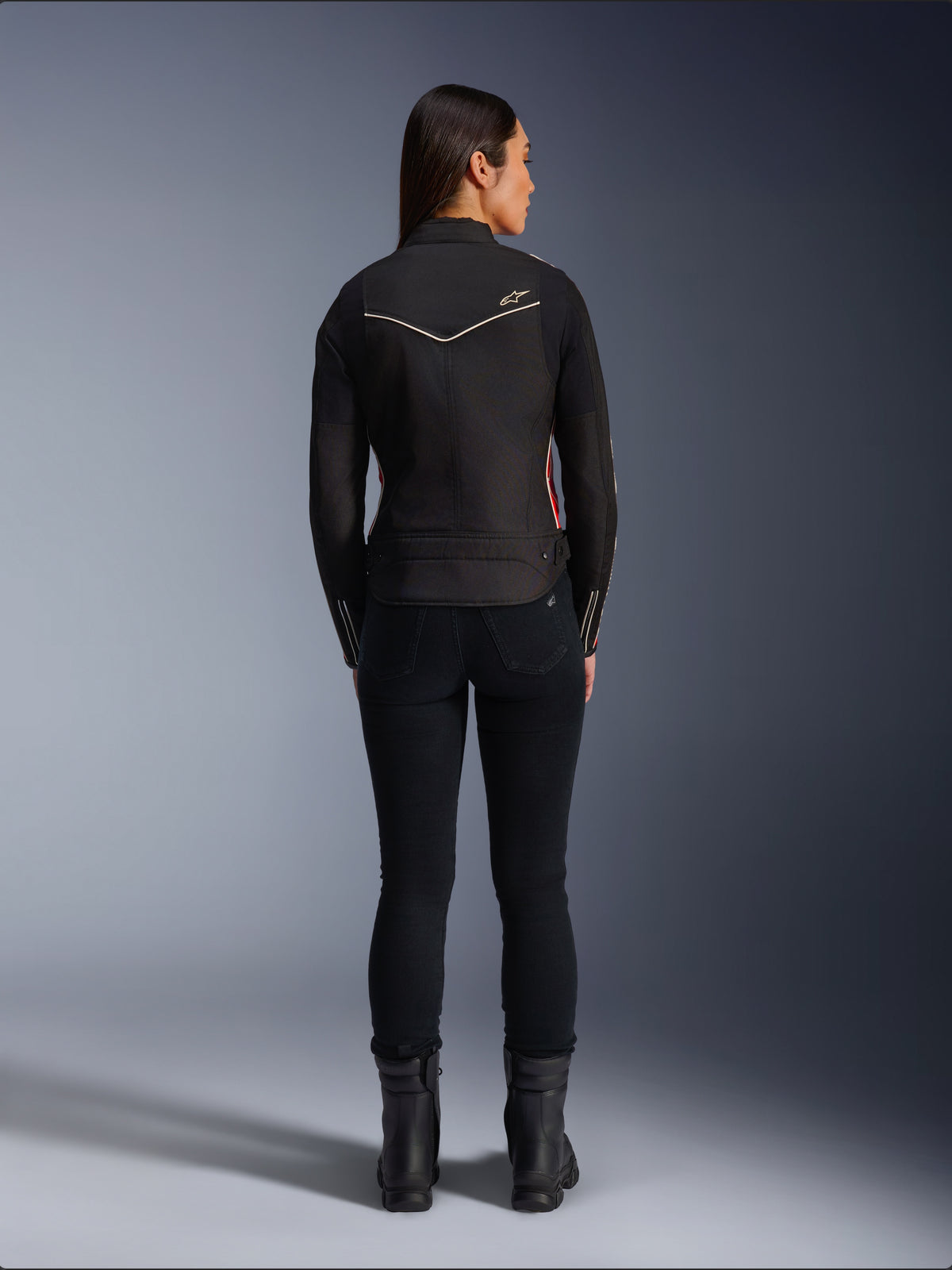 Female model from behind wearing Alpinestars Stella T-Dyno WR Jacket in Black Bright Red Fuchsia, textile motorcycle jacket with a shorter biker fit, rear view showing white star logo, styled with black pants and black boots