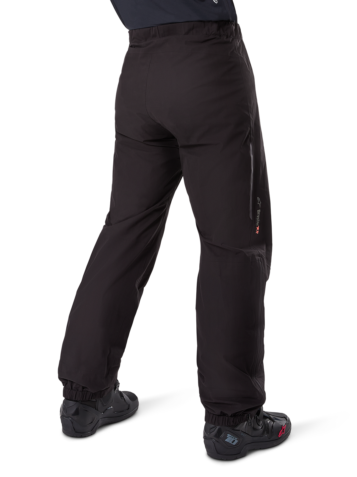 Alpinestars Amt-8 Stretch Drystar® XF Hosen-Innenfutter, Schwarz, Rückansicht zeigt das wasserdichte Futter über schwarzen Motorradstiefeln getragen, mit Drystar XF Branding am Unterschenkel, elastischen Knöchelbündchen und leichtem Stretchmaterial für Adventure-Touren.
