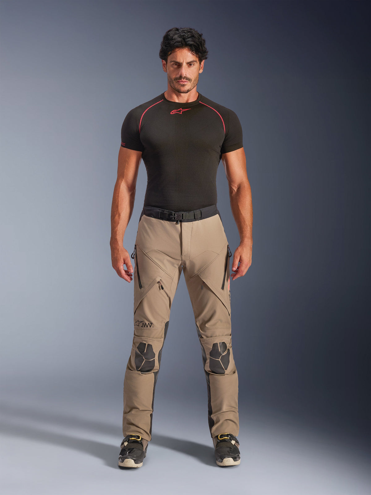 Männliches Model trägt Alpinestars AMT-8 Stretch Drystar® XF Hose in Walnut und Schwarz, kombiniert mit einem schwarzen kurzärmeligen Base-Layer, Adventure-Tourenhose mit verstärkten Knien, Belüftungsöffnungen mit Reißverschluss und ergonomischem Stretch-Design.