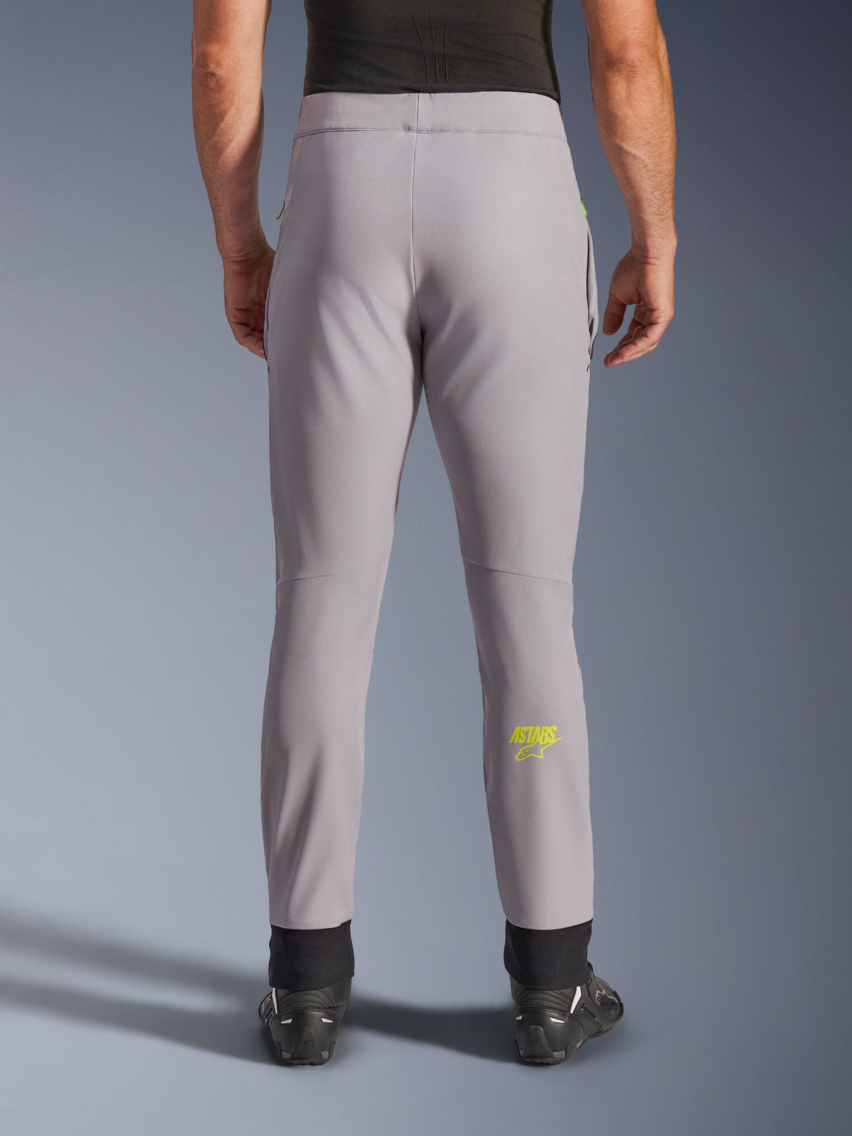 Alpinestars Aeroshell Hose, Motorradhose, Mittelgrau und Neongelb, Rückansicht mit gelbem Astars-Logo auf der Wade, schwarze elastische Knöchelbündchen, modernes Softshell-Textildesign für Straßen- und Freizeitfahrten.
