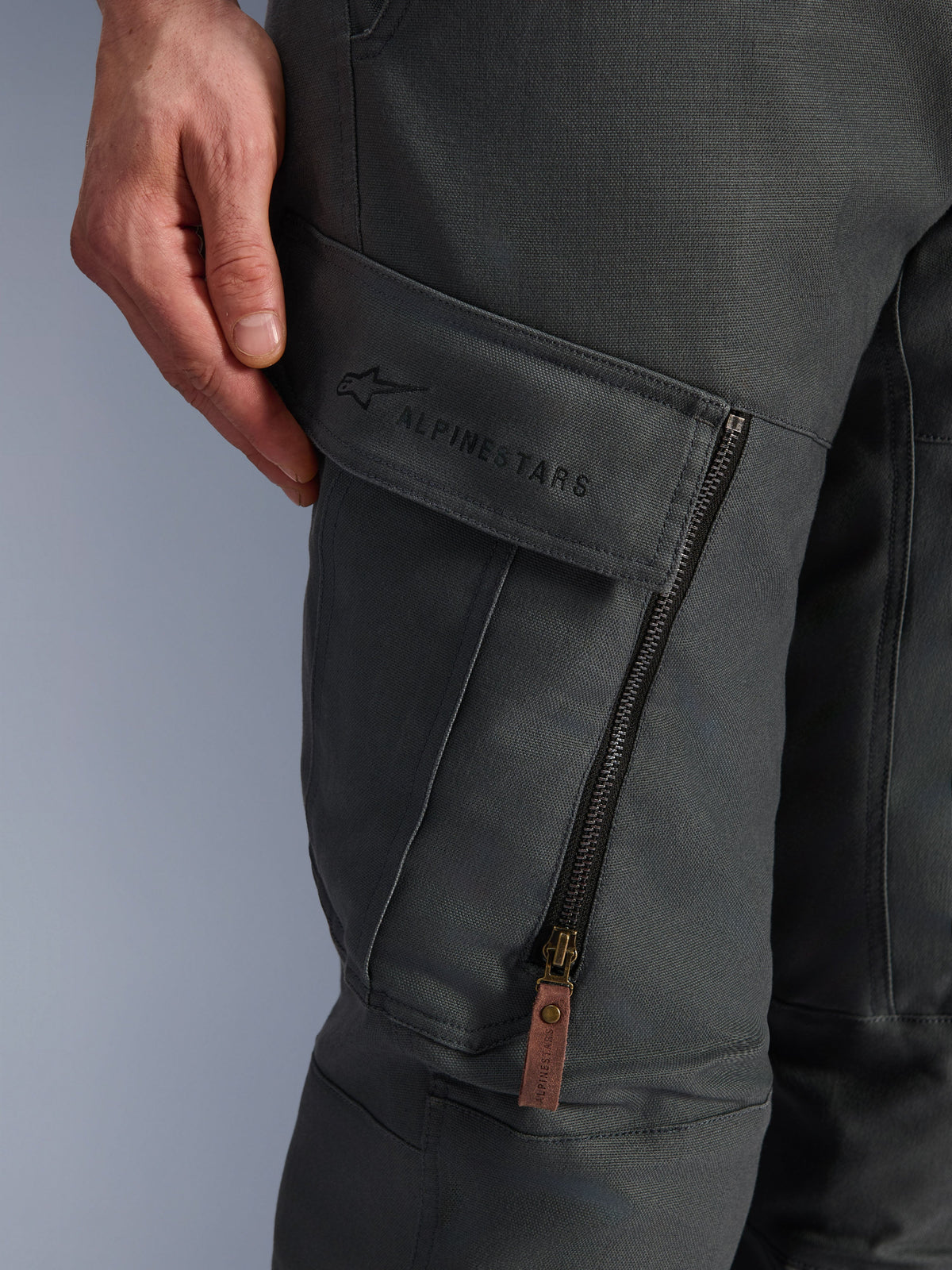 Alpinestars Borrego Drystar® Hose, Anthrazitgrau, Nahaufnahme der Cargo-Tasche am Oberschenkel mit gesticktem Markenlogo, strukturiertes, gewachstes Canvas-Material, vertikaler Belüftungsreißverschluss mit brauner Lederlasche