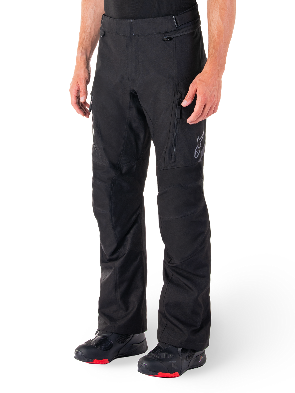 Alpinestars ST-1 Waterproof Pants, Black Motorcycle Touring Pants, worn with black and red riding boots, featuring zippered front pockets and a subtle star logo on the thigh, ergonomic design for adventure and road riding.