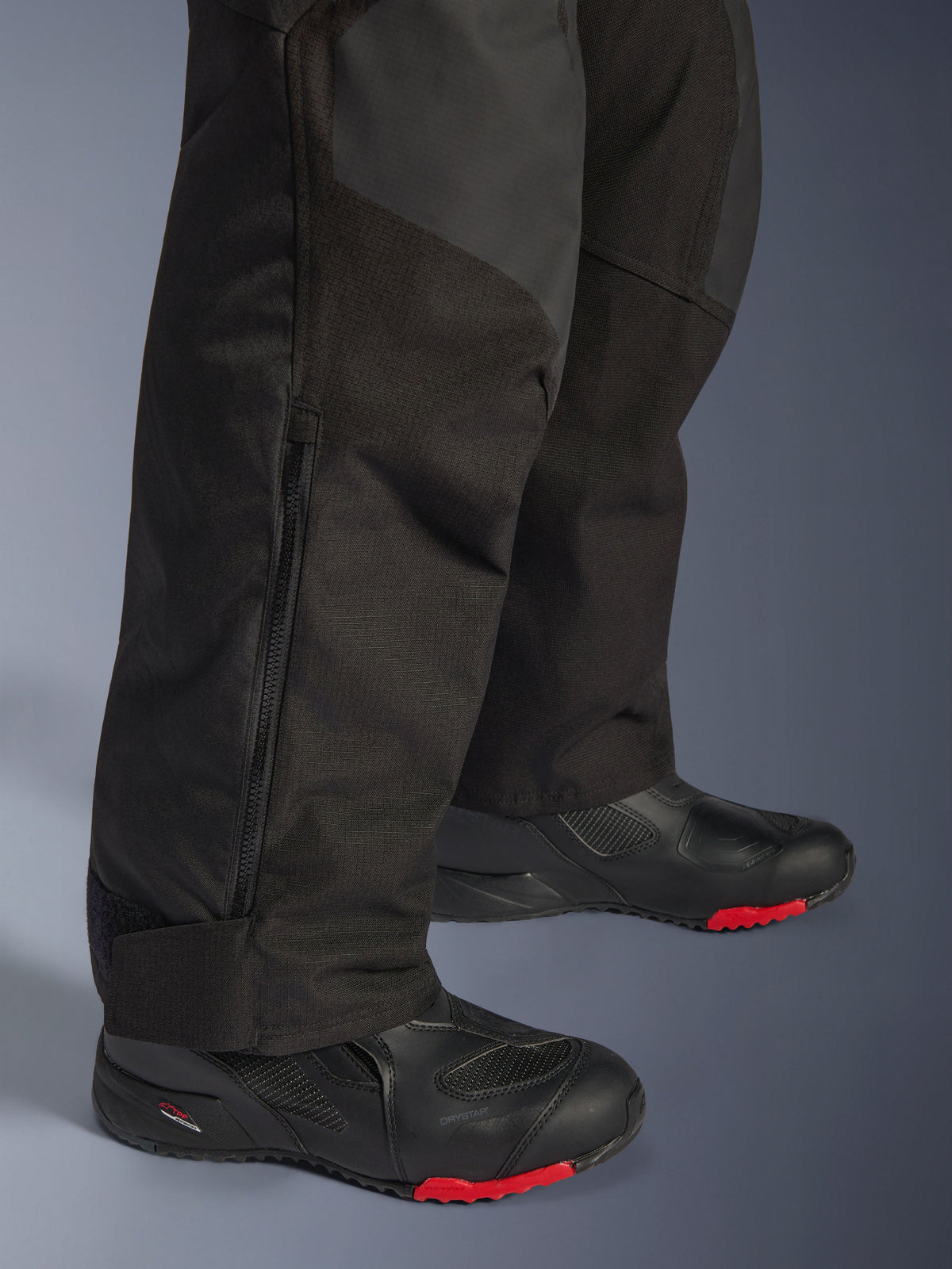 Alpinestars Andes V4 Drystar® Pants - Long, Black motorcycle adventure pants, close-up of lower leg showing adjustable zipper cuff and durable textile construction, worn with black motorcycle boots with red accents