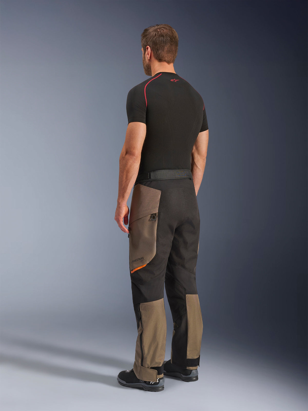 Alpinestars Cusco Drystar® Hose, Adventure-Motorradhose, Walnut Black, Rückansicht in Dreiviertel-Perspektive getragen mit schwarzem Baselayer und Stiefeln, verstärkte Textileinsätze, Cargotaschen mit Reißverschluss an den Oberschenkeln, ergonomische Touring-Passform.