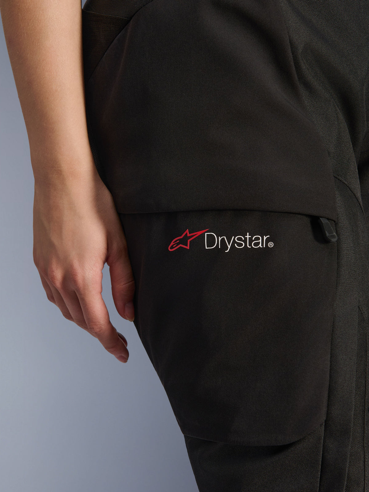 Alpinestars Stella Andes V4 Drystar® Damen-Hose, Adventure-Motorradhose, Schwarz, Nahaufnahme des Oberschenkelbereichs mit Drystar-Logo und rotem Stern-Symbol, strapazierfähiges Textilmaterial mit Cargotasche und Reißverschluss-Detail