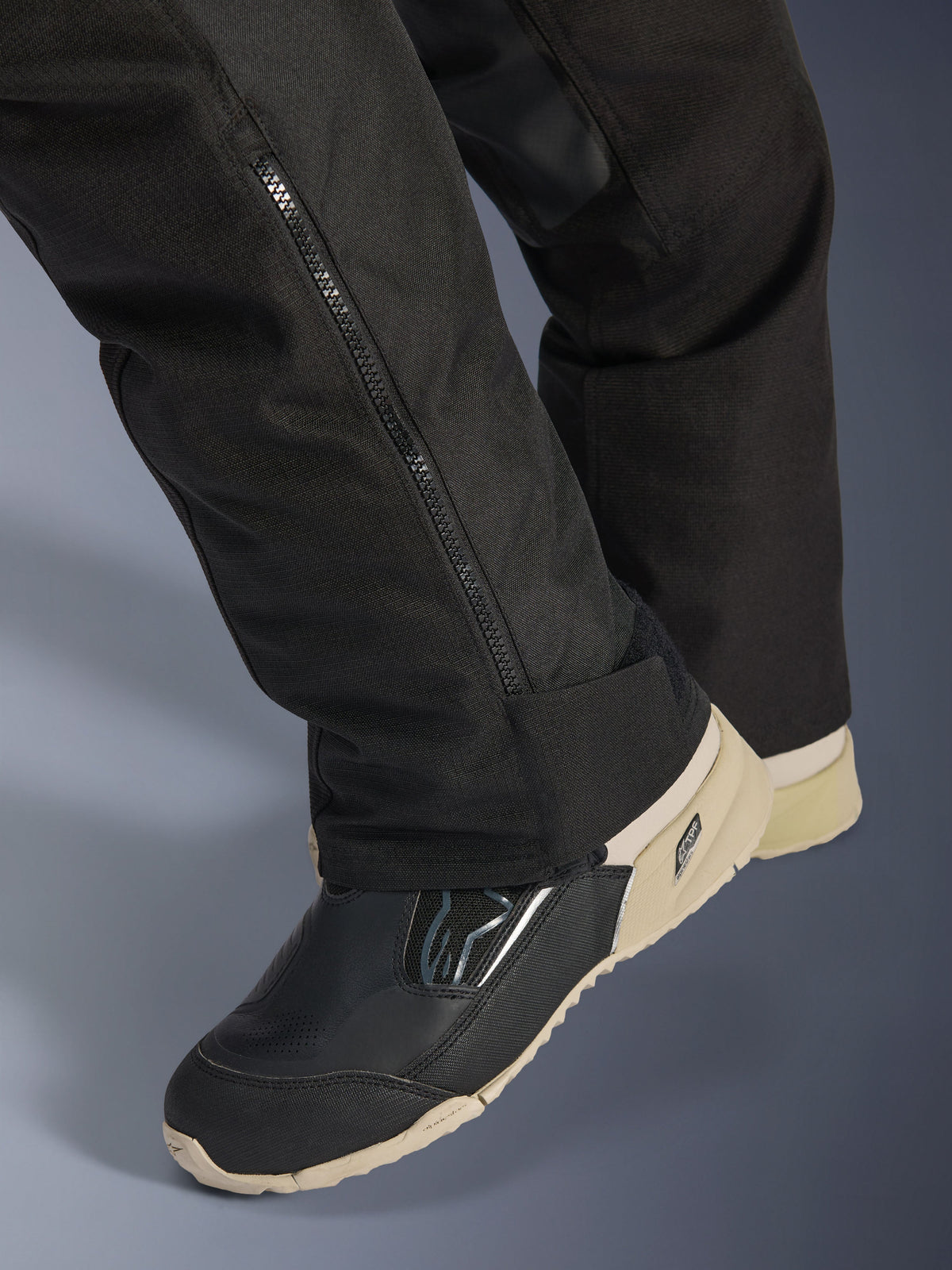 Alpinestars Stella Andes V4 Drystar® Hose, Schwarz, Nahaufnahme des unteren Hosenbeins mit seitlichem Reißverschluss zur Stiefelanpassung, strapazierfähiges Textilmaterial, getragen mit schwarz-beigen Motorradstiefeln, abenteuertaugliches funktionales Design