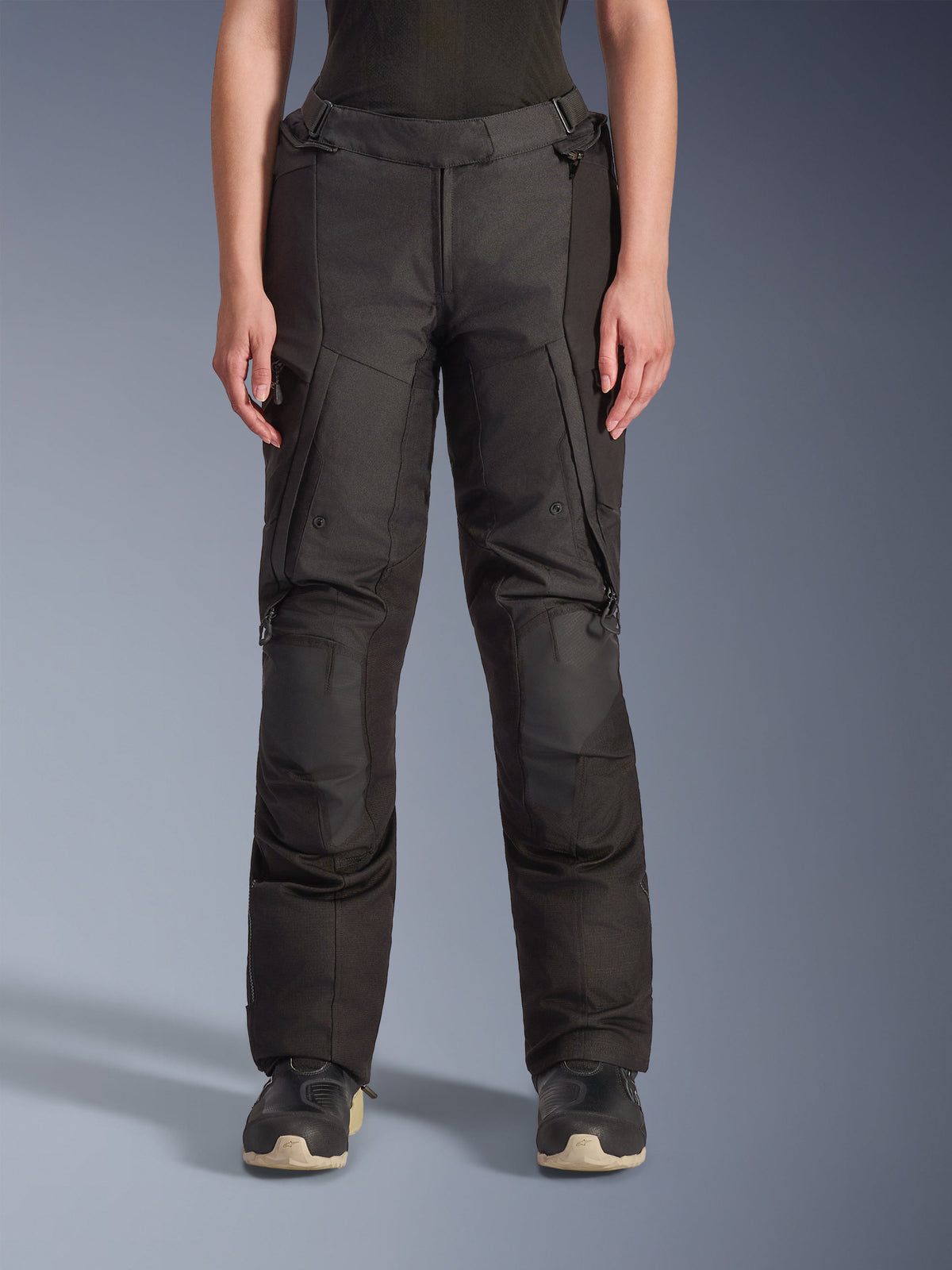 Alpinestars Stella Andes V4 Drystar® Hose, Damen-Adventure-Tourenhose, Schwarz, Vorderansicht, mit verstärkten Knieeinsätzen, wasserabweisenden Cargotaschen und verstellbaren Taillenriemen, getragen mit schwarzen Stiefeln in einer Studioumgebung.