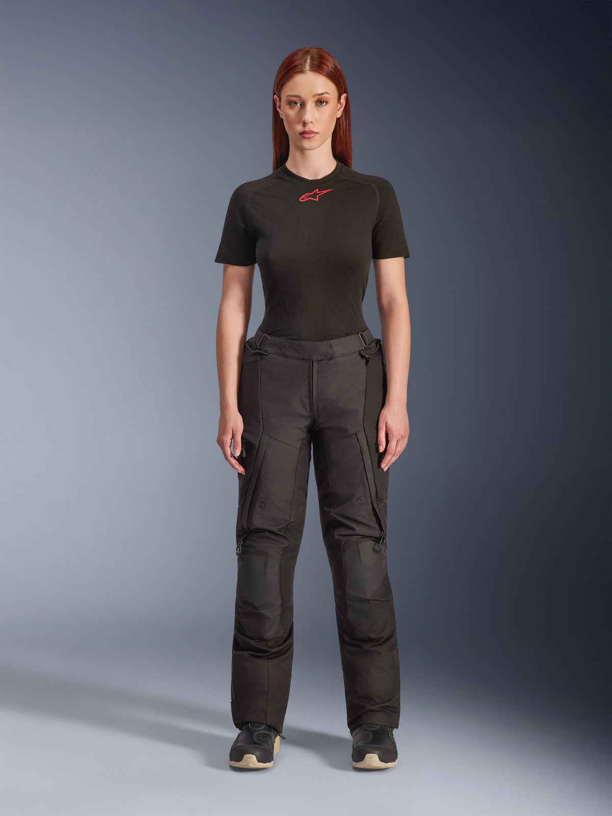 Alpinestars Stella Andes V4 Drystar® Hose, schwarze Adventure-Touring-Motorradhose für Damen, präsentiert an einem Modell mit einem schwarzen Alpinestars T-Shirt, technisches Textildesign mit Cargotaschen und verstärkten Knieeinsätzen.