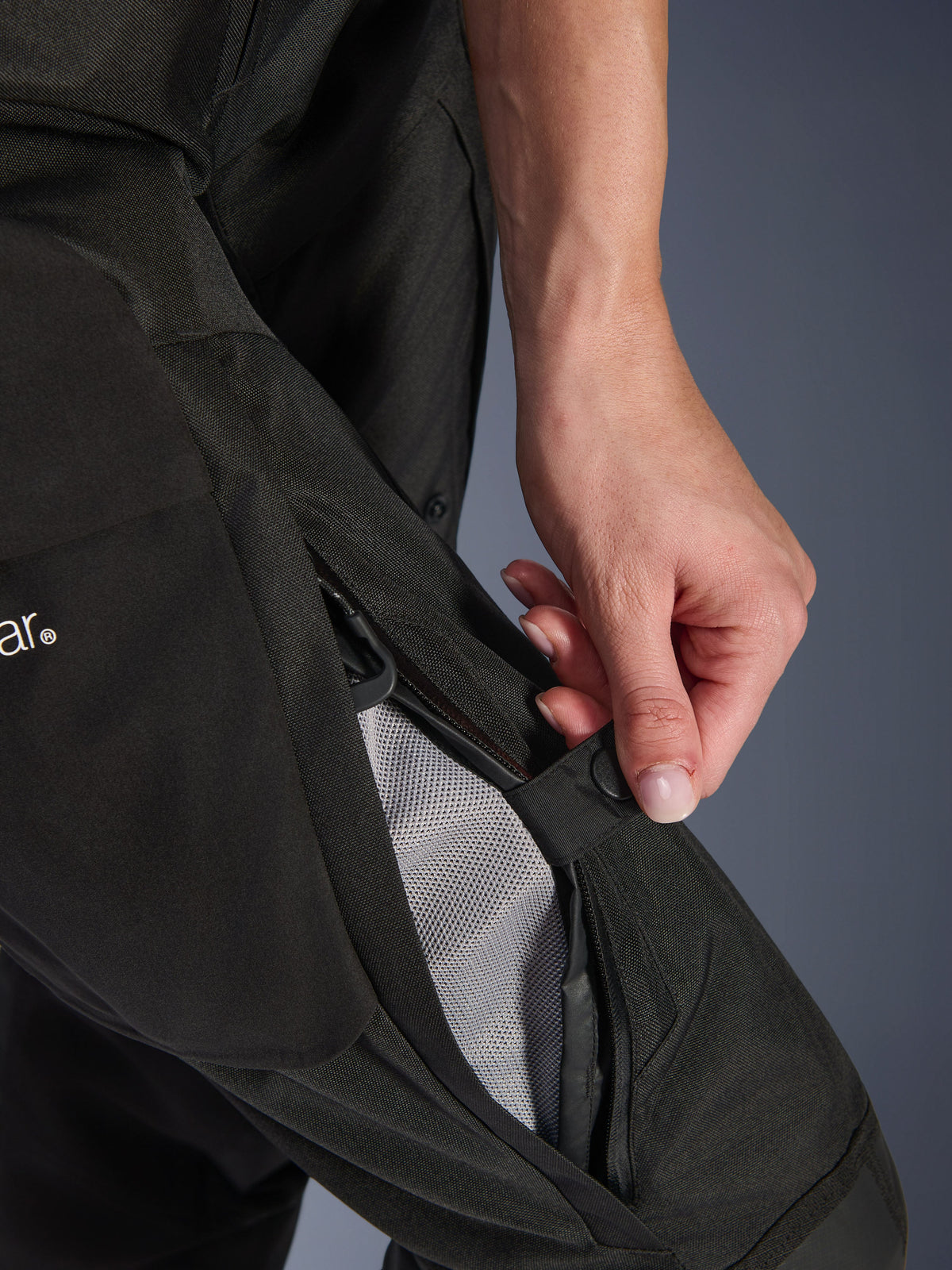 Alpinestars Stella Andes V4 Drystar® Damen-Hose, Motorradhose, Schwarz, Nahaufnahme einer Hand beim Öffnen der Oberschenkelbelüftung mit Reißverschluss, um das Mesh-Futter für die Luftzirkulation freizulegen, strapazierfähige Adventure-Textilausrüstung