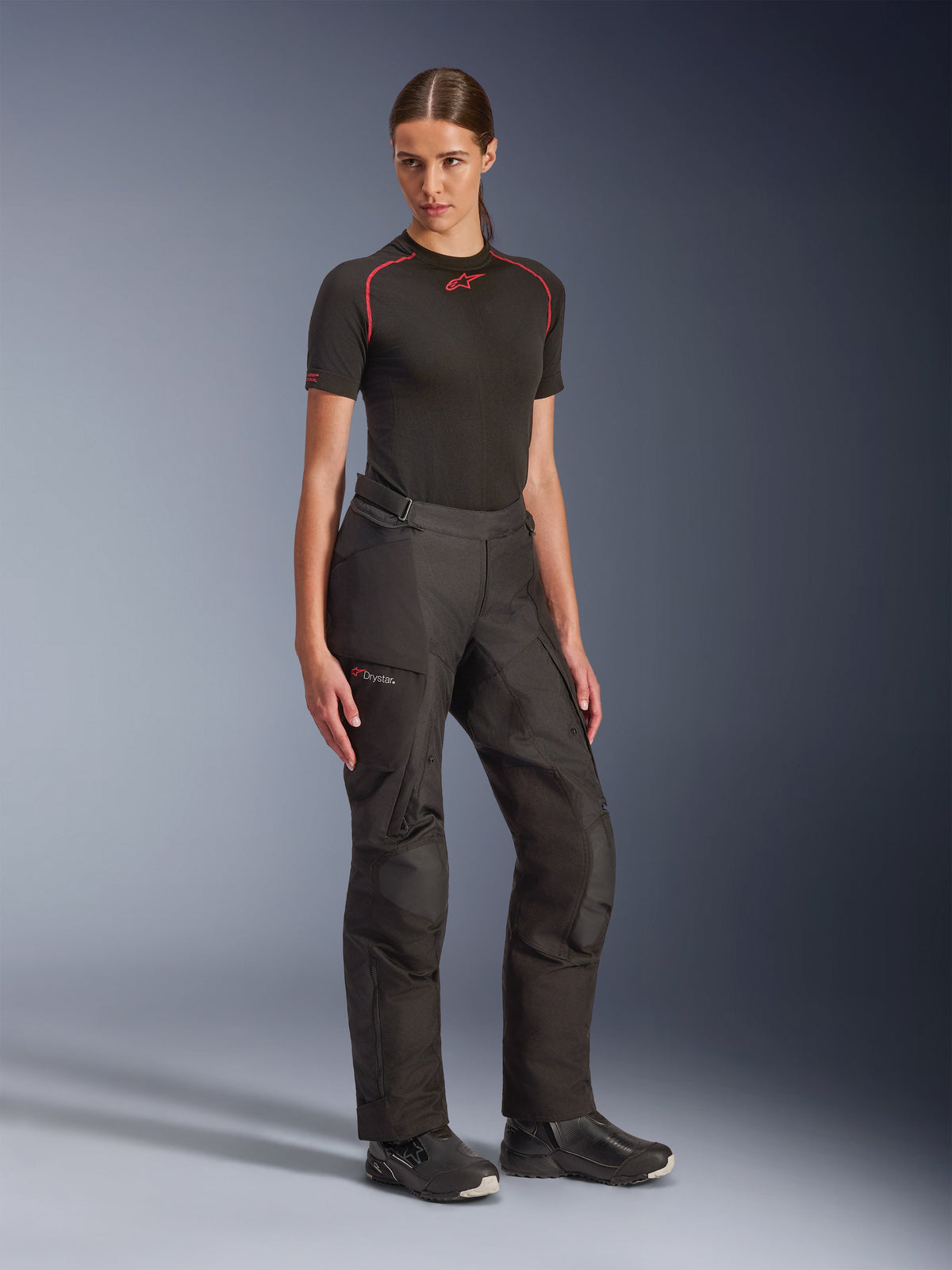 Alpinestars Stella Andes V4 Drystar® Hose, Schwarz, Adventure-Touring-Motorradhose für Damen, getragen mit einem schwarzen kurzärmeligen Baselayer und schwarzen Motorradstiefeln, mit wasserdichter Drystar-Technologie und Cargotaschen.