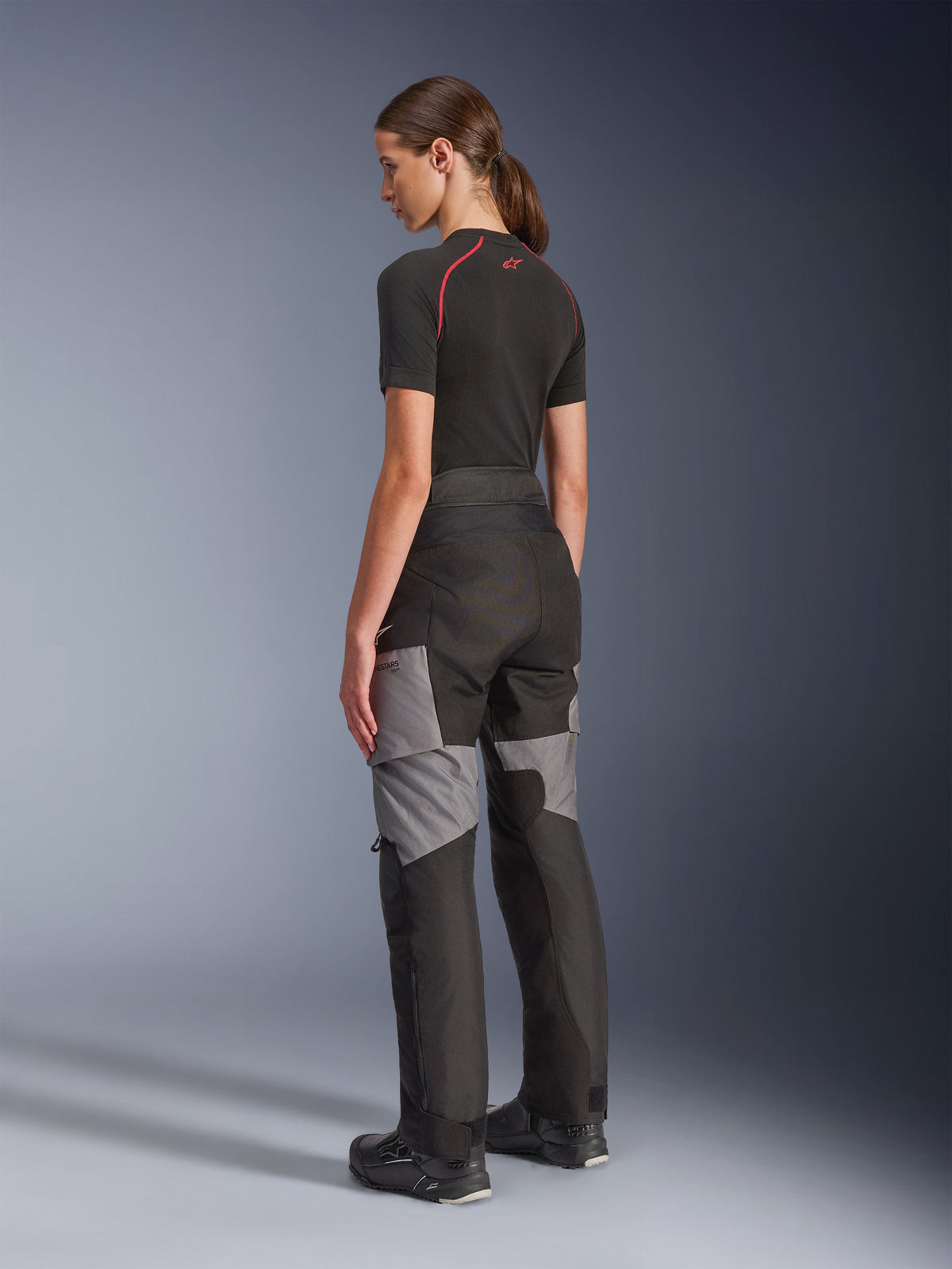 Woman Stella Andes V4 Drystar® Pants, Black and Dark Gray motorcycle adventure-touring pants, back and side view on model, featuring durable textile construction with gray reinforcement panels and a tailored fit for women riders.