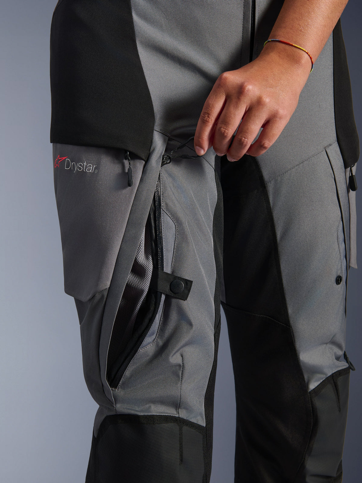 Alpinestars Stella Andes V4 Drystar Pants, Black and Dark Gray textile, close-up of direct thigh ventilation zipper being opened by hand, mesh lining visible, featuring Drystar logo, adventure motorcycle riding gear
