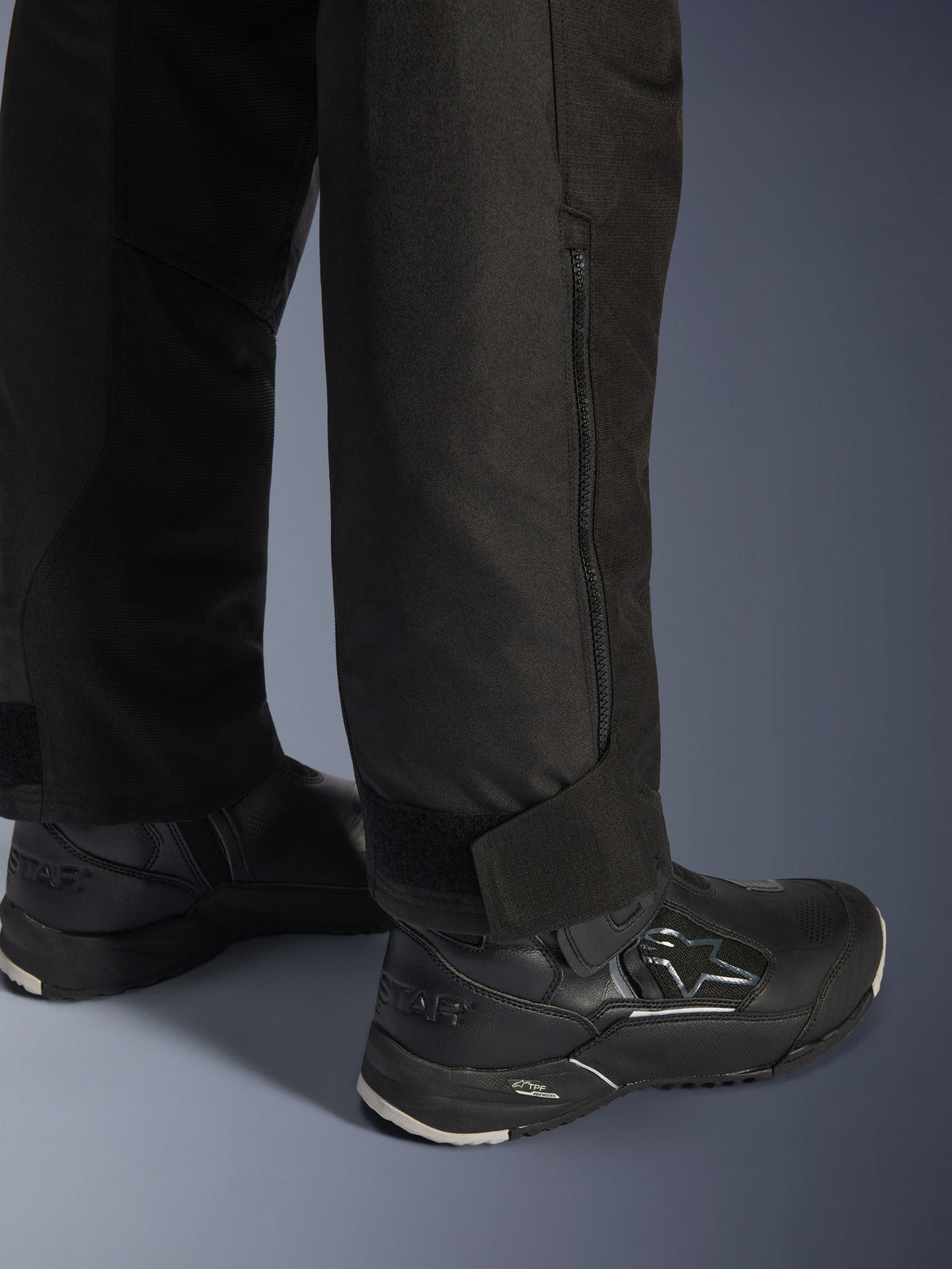Alpinestars Stella Andes V4 Drystar® Pants, Black, close-up view of the lower leg and cuff, featuring a side zipper and adjustable hook-and-loop ankle strap, worn with black Alpinestars riding boots