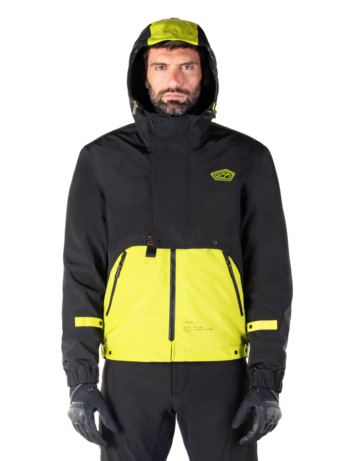 Alpinestars Mootant Waterproof Parka, Lime Punch Black motorcycle jacket, front view, modular 3-in-1 design with black upper and bright lime green lower section, featuring a drawstring hood and chest logo, worn with black pants and riding gloves