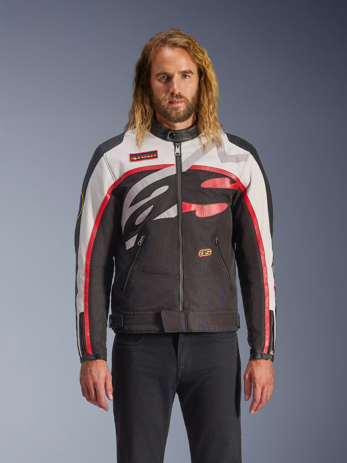Alpinestars Axton Jacke, Motorradjacke, Schwarz, Off-White und leuchtendes Rot, mit markanten abstrakten Mustern auf der Brust und umlaufendem Logo, rot gestreifte Ärmel, Vintage-inspiriertes Design mit minimalistischem Kragen, getragen von einem Model mit schwarzen Jeans.