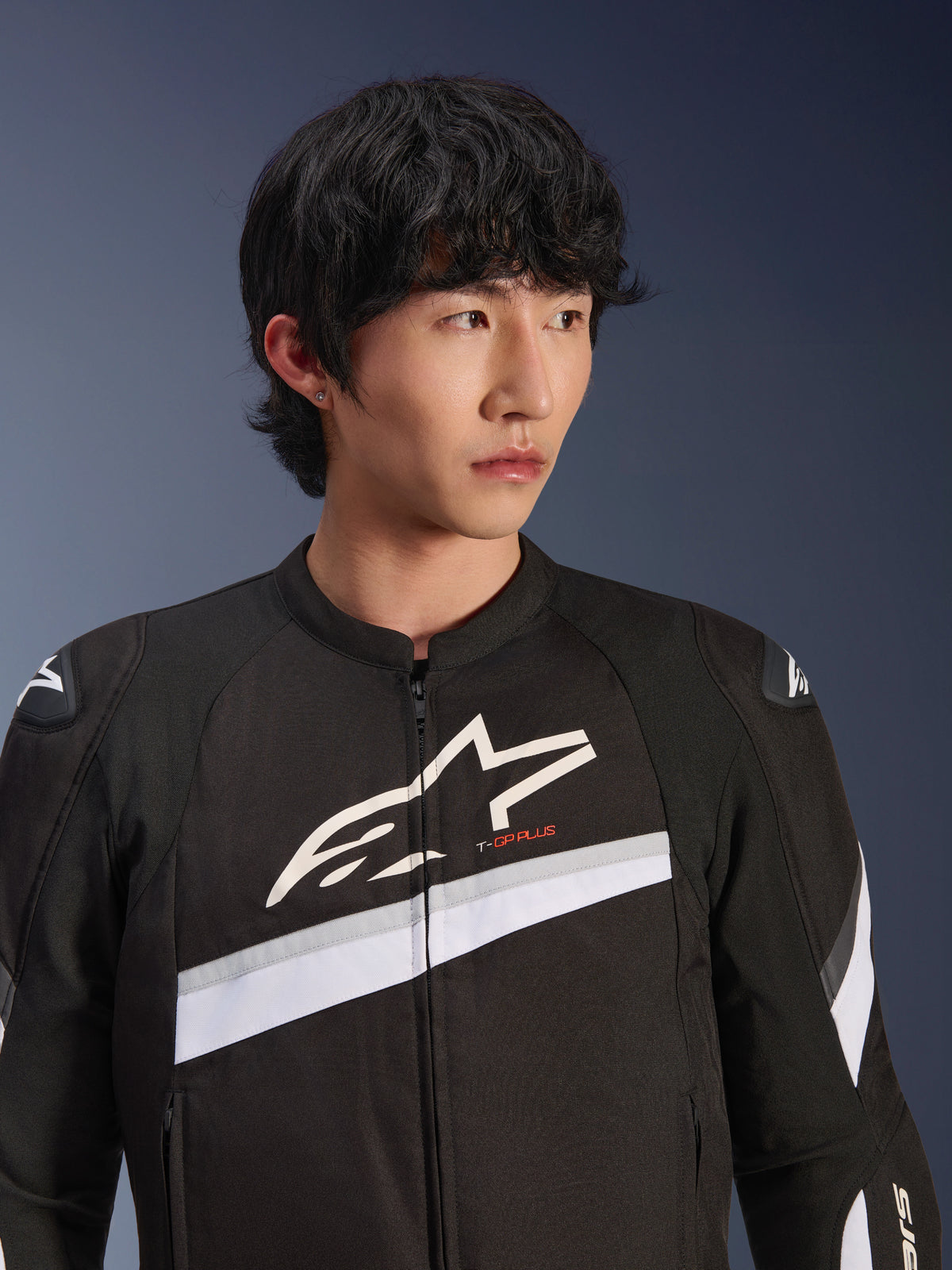 Alpinestars T-GP Plus R V4 Jacke, Schwarz und Weiß, Textil-Motorradjacke getragen von einem männlichen Model, großes weißes Stern-Logo auf der Brust, weiße diagonale Streifen, DFS Lite Schulterprotektoren, sportlich inspirierte Street-Riding-Ausrüstung.