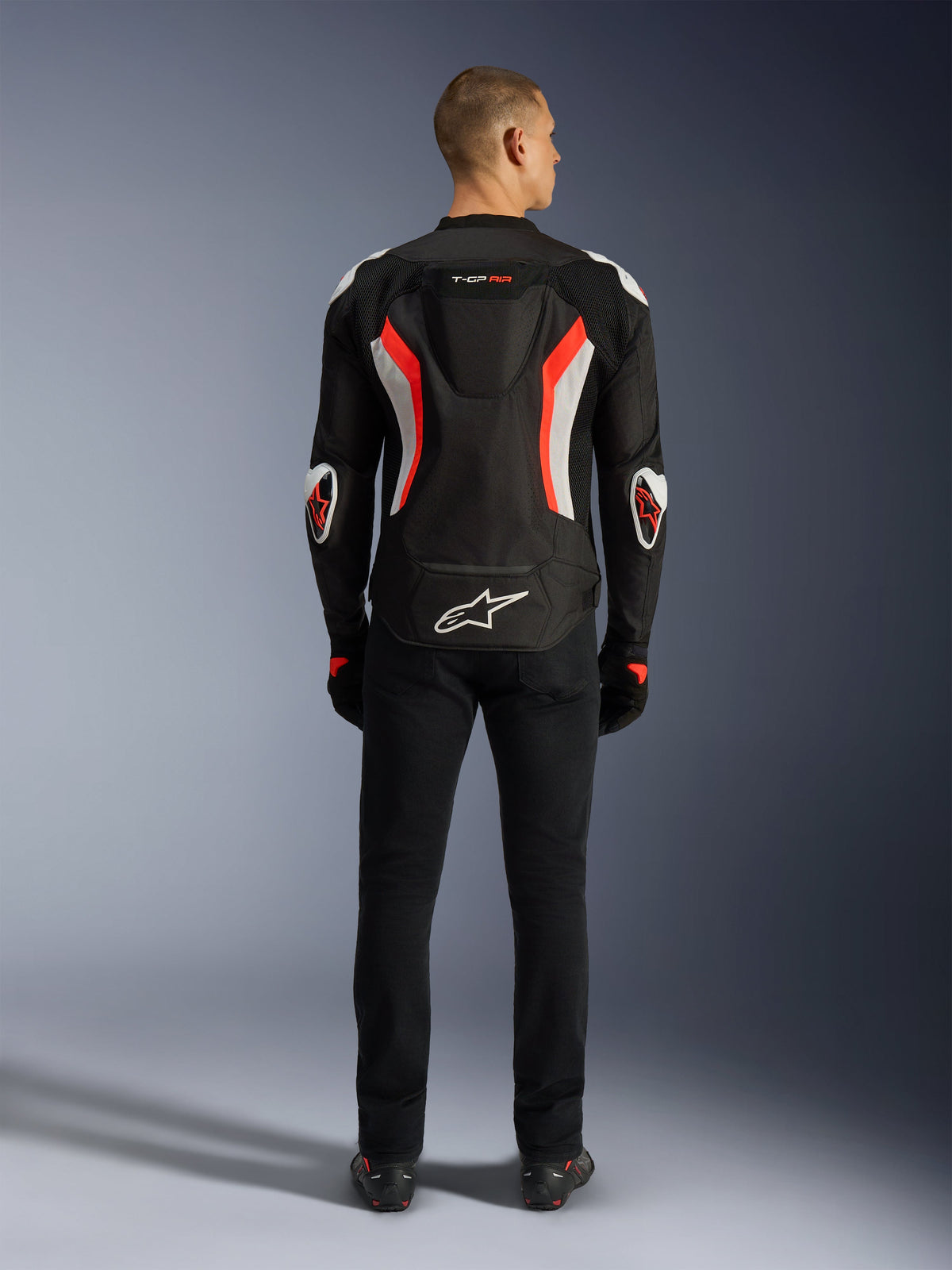 Alpinestars T-GP Air Jacke, Motorradjacke, Schwarz Rot Fluo, Rückansicht an einem Modell, mit aerodynamischem Höcker, weißen und leuchtroten Akzenten, Alpinestars-Logo am unteren Rücken, sportlicher Schnitt für den Straßeneinsatz