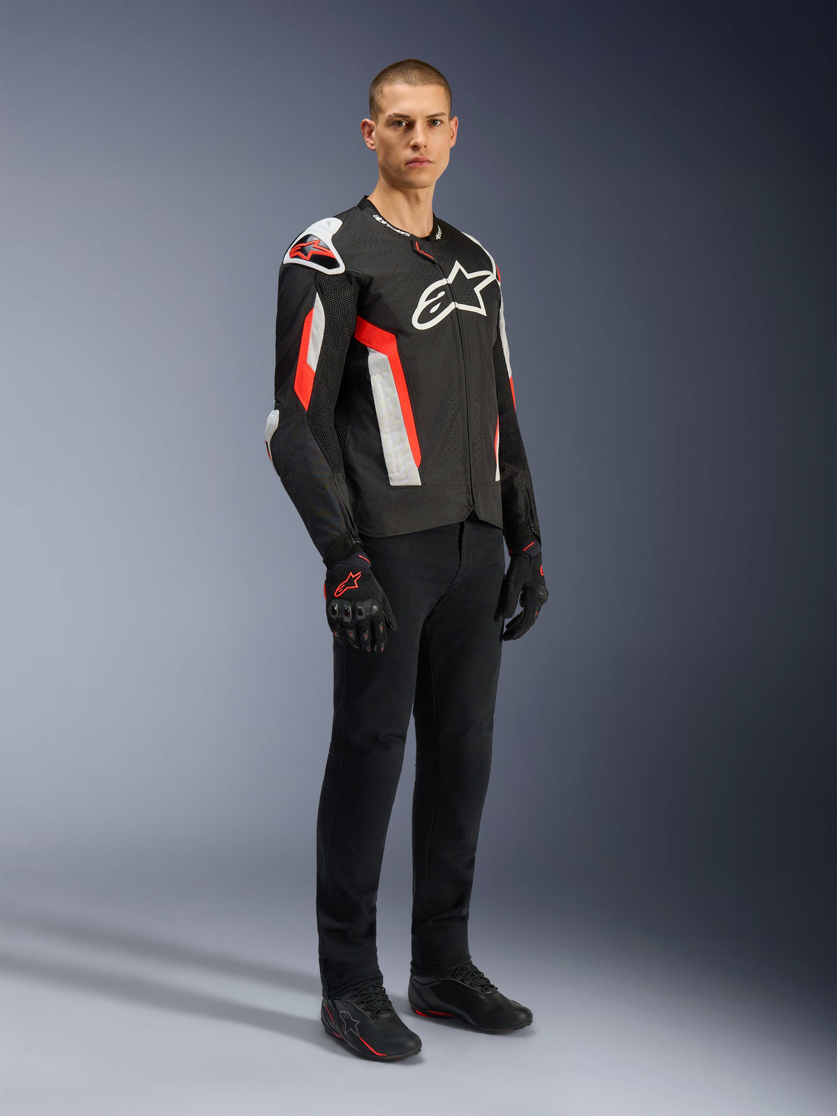 Alpinestars T-GP Air Jacke, Schwarz Rot Fluo, getragen von Model mit schwarzer Motorradhose und Handschuhen, mit laserperforierten Textilpaneelen, weißem Alpinestars-Branding und roten Akzenten, Sport-Motorradjacke für Straßenfahrten bei warmem Wetter