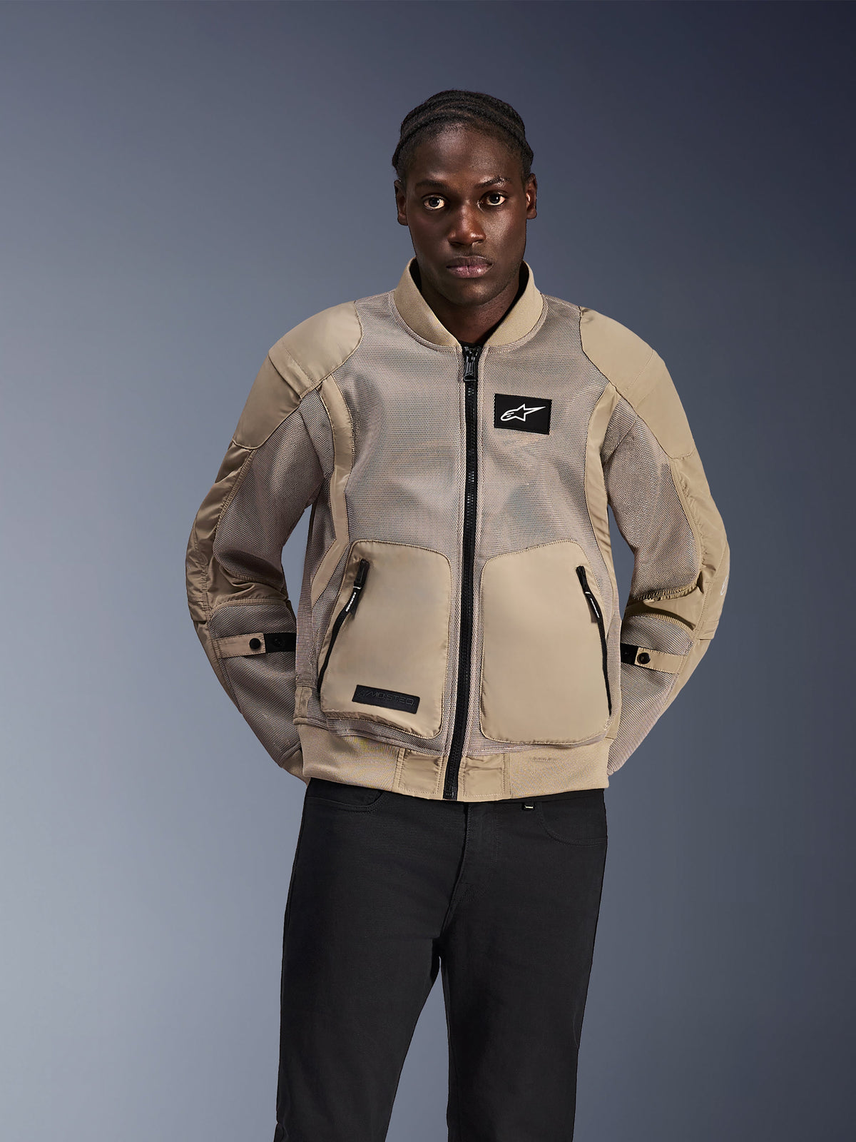 Alpinestars Flight Air Jacke, urbane Motorradjacke im Bomber-Stil, Hellbraun, mit großflächigen 3D-Mesh-Einsätzen zur Belüftung und großen Fronttaschen, getragen von einem Mann mit schwarzer Hose, modernes motorsport-inspiriertes Design für Fahrten bei heißem Wetter