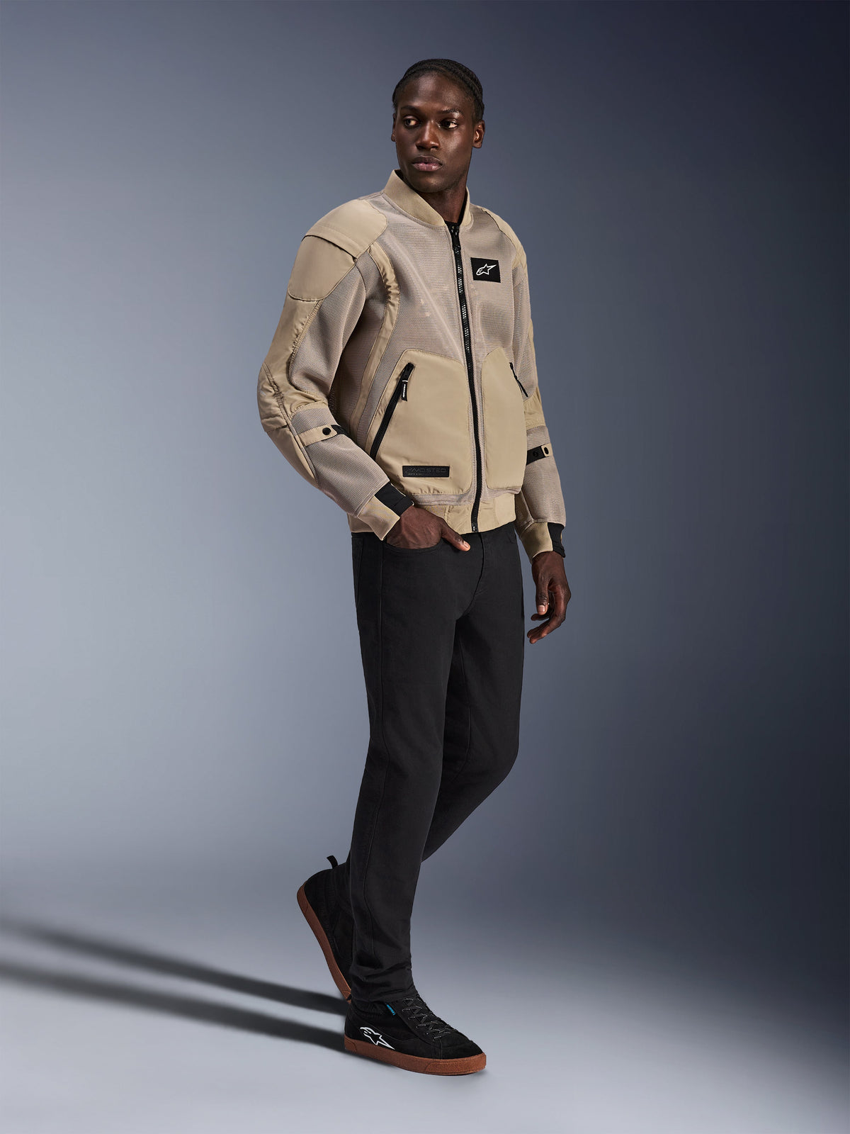 Alpinestars Flight Air Jacke, urbane Motorradjacke, Farbe Aluminum, von einem Model mit schwarzer Hose und schwarzen Sneakern getragen, mit 3D-Mesh-Belüftungseinsätzen und Design im Bomber-Stil, moderner Streetstyle für urbane Fahrten.