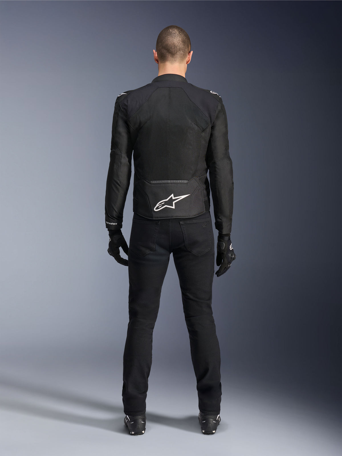Alpinestars Viper Air V4 Jacke, schwarze Textil-Motorradjacke, Rückansicht mit weißem Alpinestars Stern-Logo auf dem unteren Rücken, kombiniert mit schwarzer Motorradhose und Handschuhen, Sommerausrüstung für Straßen- und Sportfahrten
