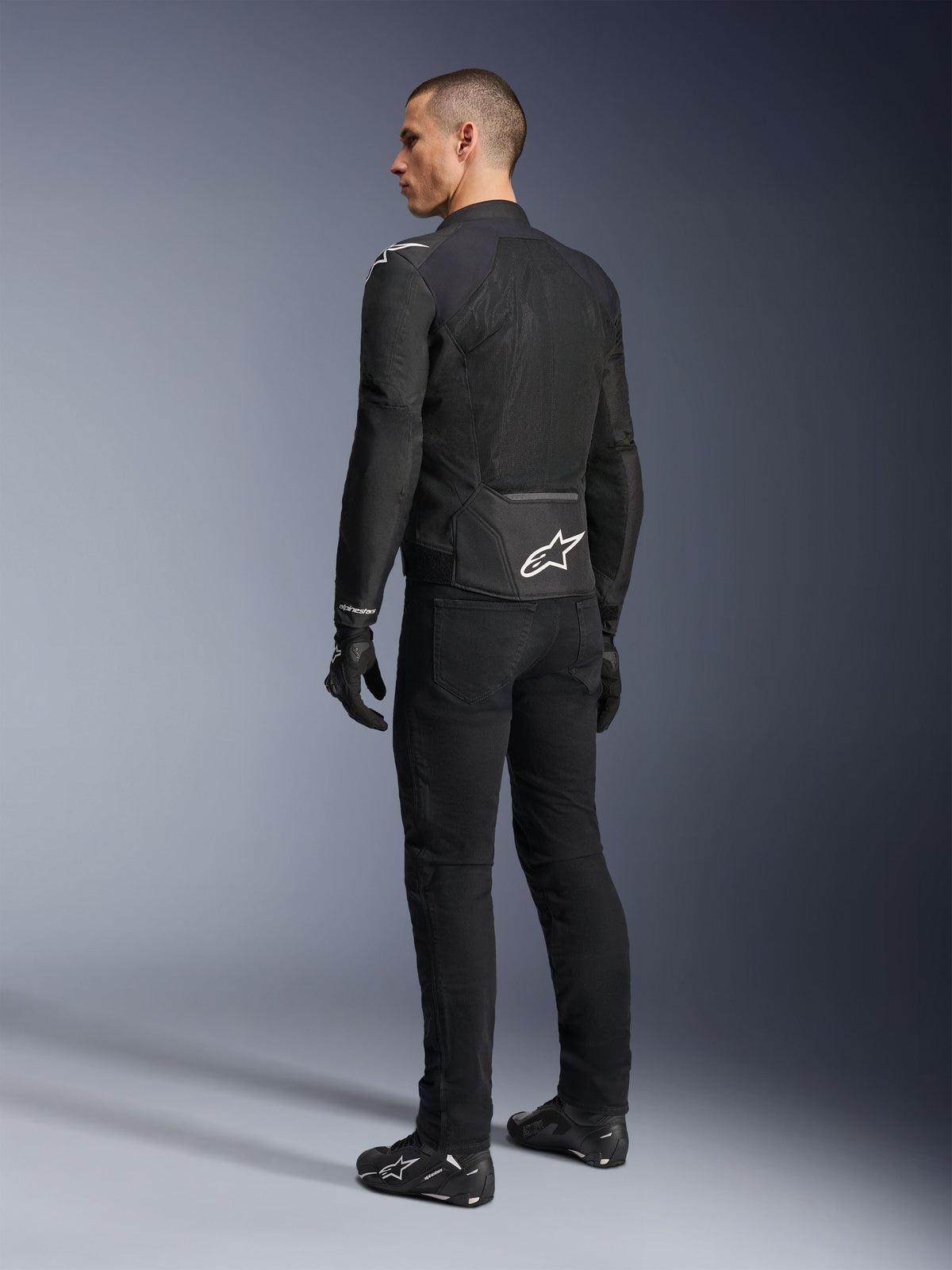 Alpinestars Viper Air V4 Jacke, schwarze Textil-Motorradjacke, Rückansicht an einem männlichen Model, mit großen Tech-Mesh-Einsätzen für Luftzirkulation und weißem Stern-Logo auf dem unteren Rücken, getragen mit passender schwarzer Motorradhose und Handschuhen