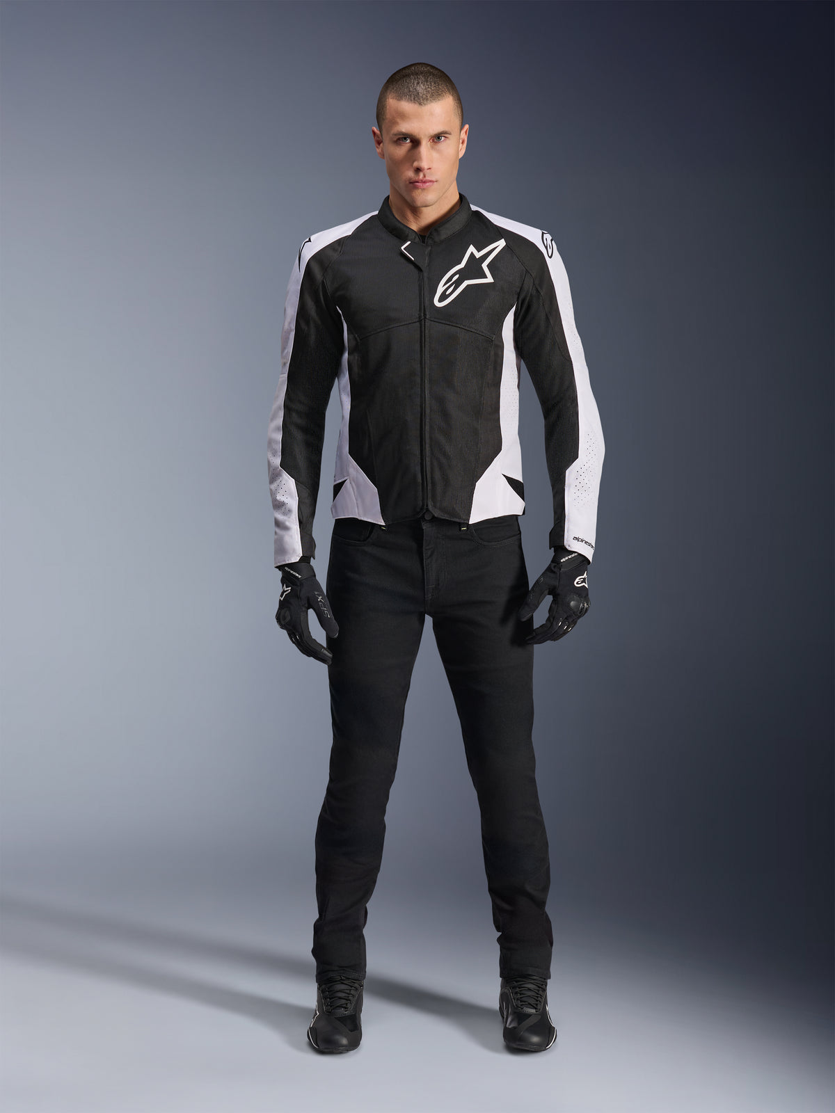 Alpinestars Viper Air V4 Jacke, schwarz-weiße Motorradjacke mit großem weißem Logo auf der Brust, getragen von einem männlichen Model mit schwarzer Hose und Handschuhen, mit Mesh-Panels zur Belüftung, sportliche Straßenmotorradbekleidung