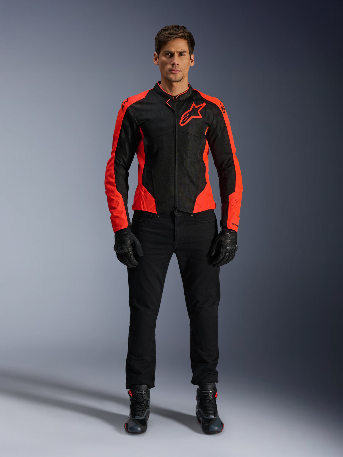 Männliches Model trägt die Alpinestars Viper Air V4 Jacke in Rot Fluo und Schwarz, kombiniert mit schwarzer Motorradhose, Handschuhen und Stiefeln, mit atmungsaktiven Mesh-Einsätzen zur Belüftung und einem markanten Stern-Logo auf der Brust, sportliche Motorrad-Straßenbekleidung
