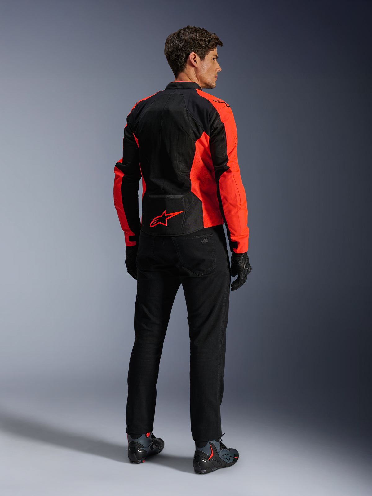 Alpinestars Viper Air V4 Jacke, Red Fluo Black, Rückansicht am Modell, mit technischen Mesh-Einsätzen und einem roten Stern-Logo am unteren Rücken, kombiniert mit schwarzer Motorradhose und Handschuhen für einen kompletten Road-Riding-Look.