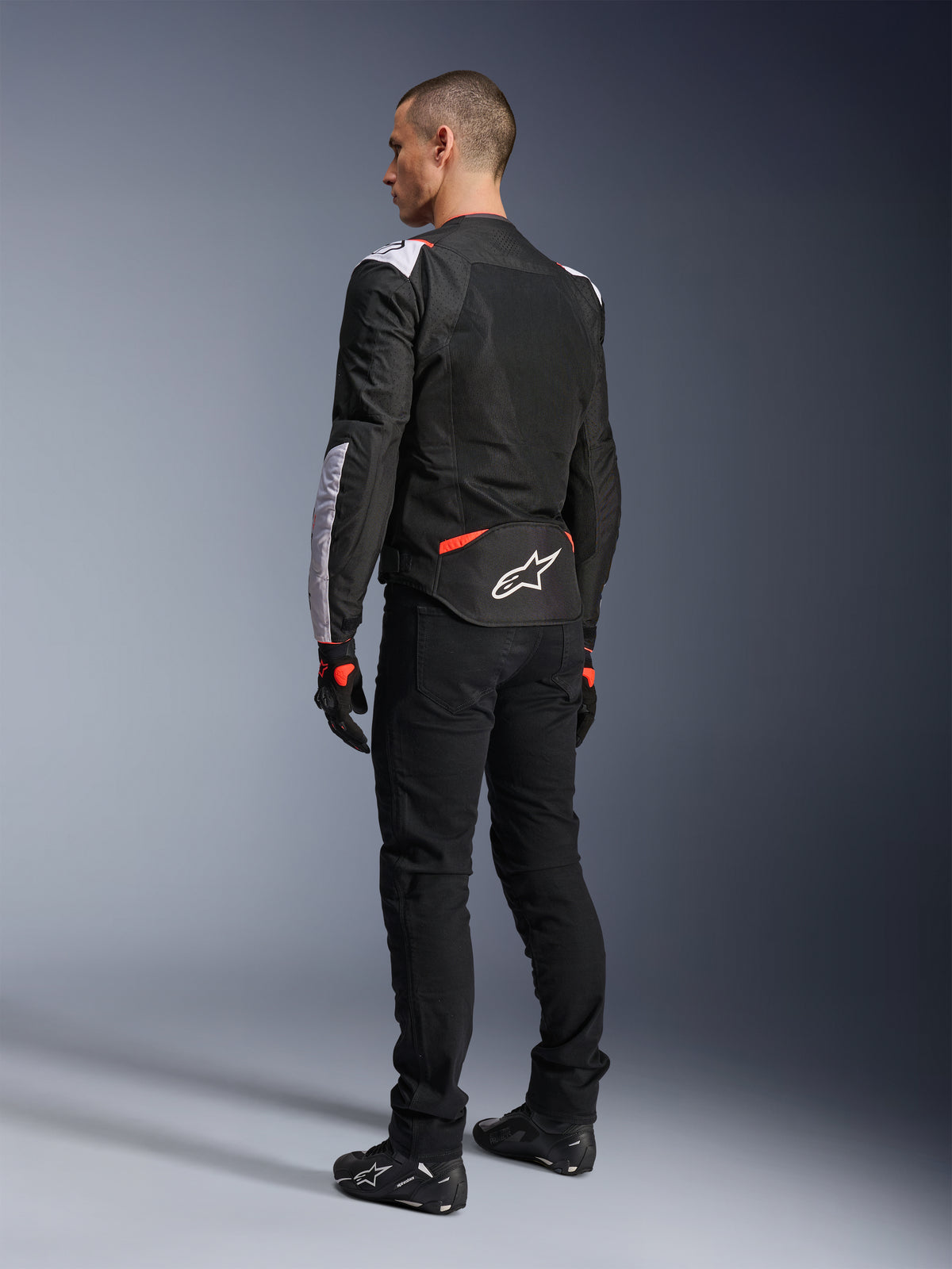 Alpinestars T-Sps Air V2 Jacke, Textil-Motorradjacke, Schwarz, Weiß und Fluo-Rot, Rückansicht am Modell, Mesh-Einsätze für Belüftung, weißes Astars-Logo am unteren Rücken, kombiniert mit schwarzer Motorradhose und Handschuhen