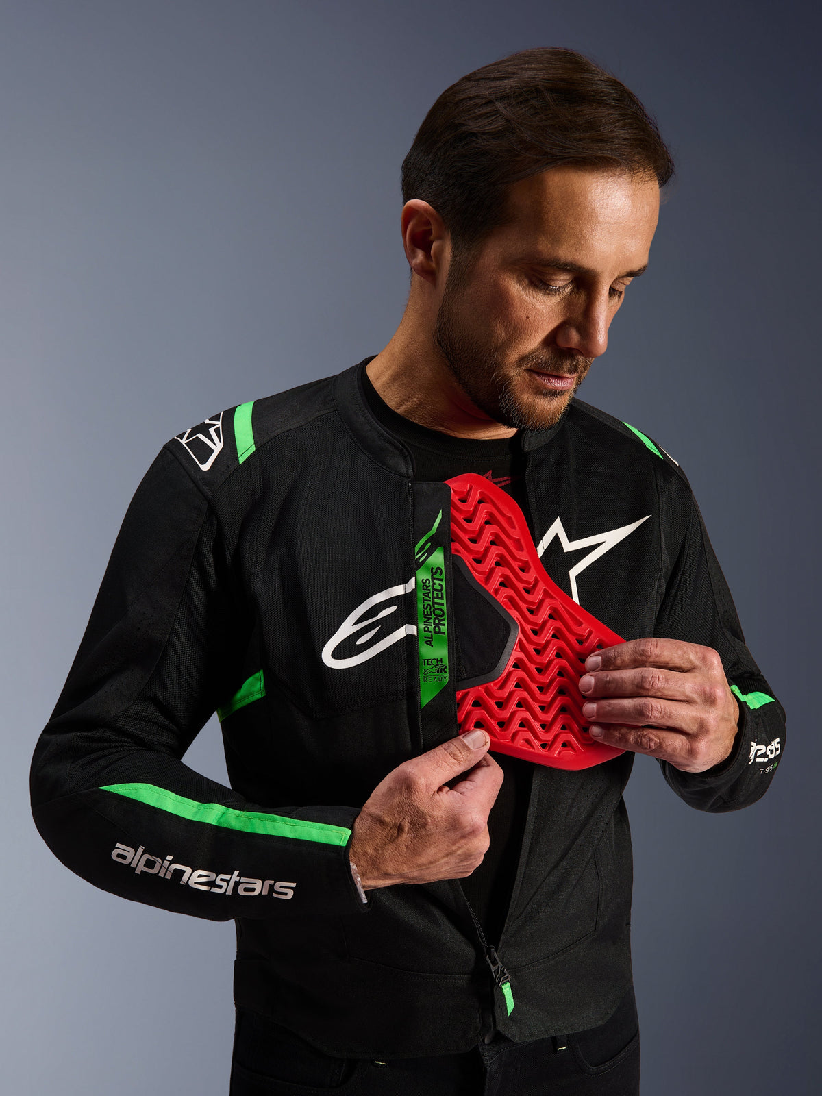Alpinestars T-SPS Air V2 Jacket, Black Fluo Green motorcycle jacket, man demonstrating red Nucleon chest protector insert, Tech-Air Ready label, sporty textile design with mesh panels