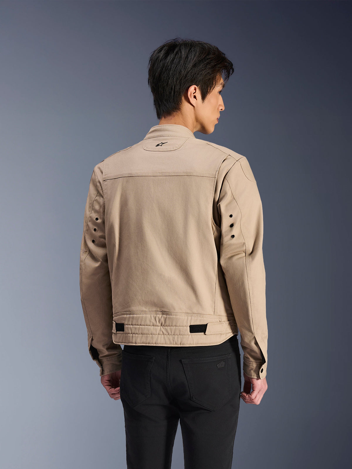 Alpinestars Bruiser Jacket, Brown urban motorcycle jacket, rear view showing articulated pleated shoulders and adjustable waist straps, worn with black pants, contemporary workwear-inspired riding gear
