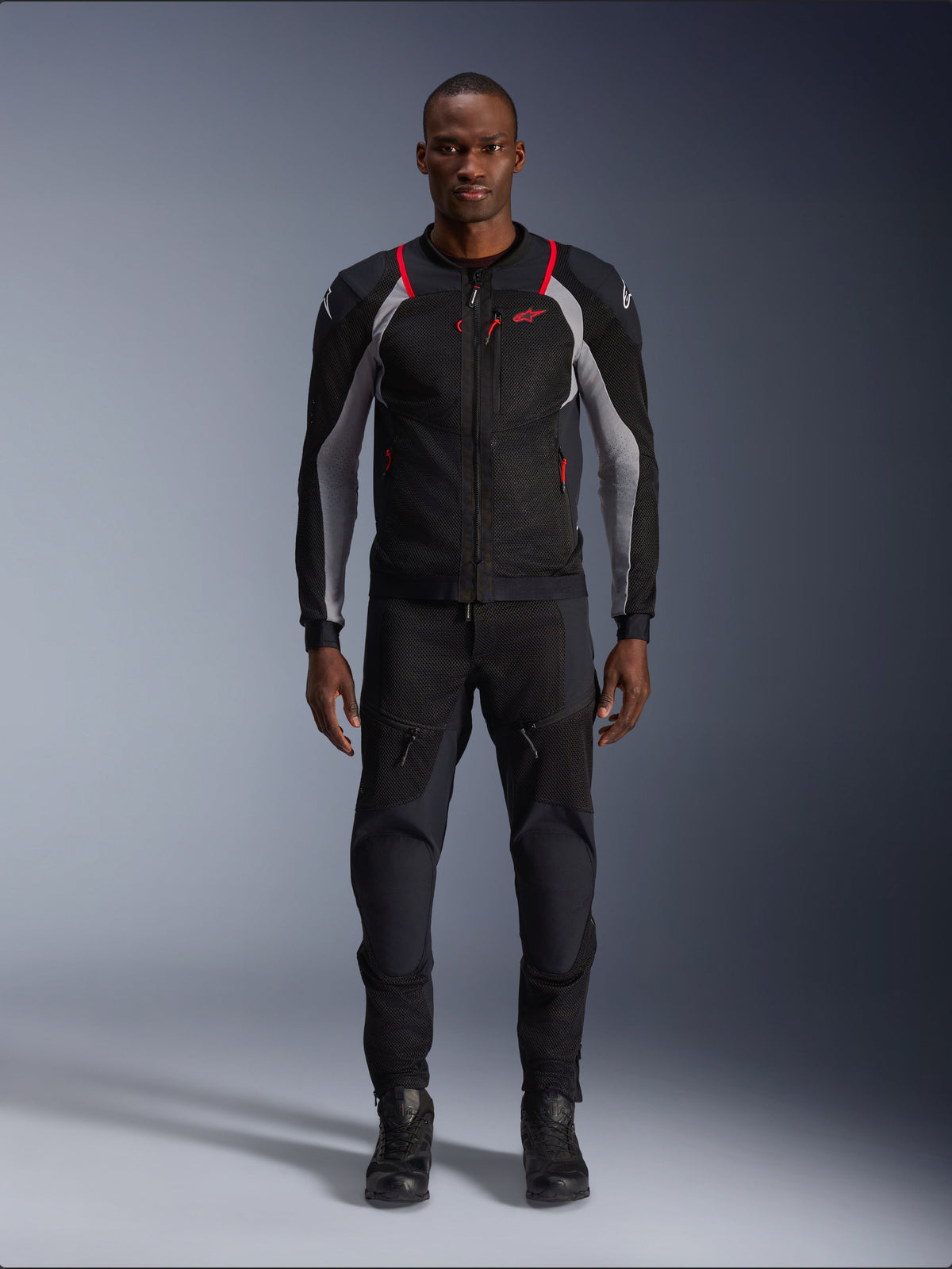 Alpinestars Troop-Air Pro Jacke, technische Motorradjacke, Black Ash Gray und Bright Red, mit Mesh-Einsätzen und roten Akzenten, getragen von einem männlichen Model mit schwarzer Motorradhose und Stiefeln, elegantes urbanes Design mit technischer Belüftung.