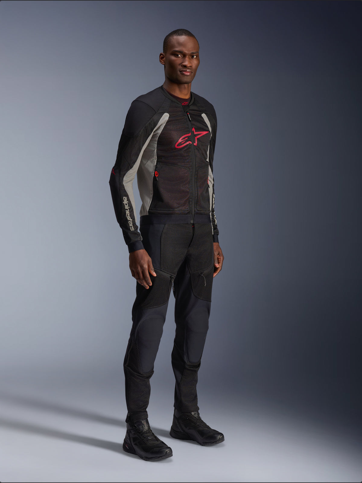 Alpinestars Troop-Air Jacket, technical mesh motorcycle jacket in Black, Ash Gray and Bright Red, worn by a model with matching black pants and boots, featuring a red Alpinestars logo on the chest, urban contemporary riding gear.