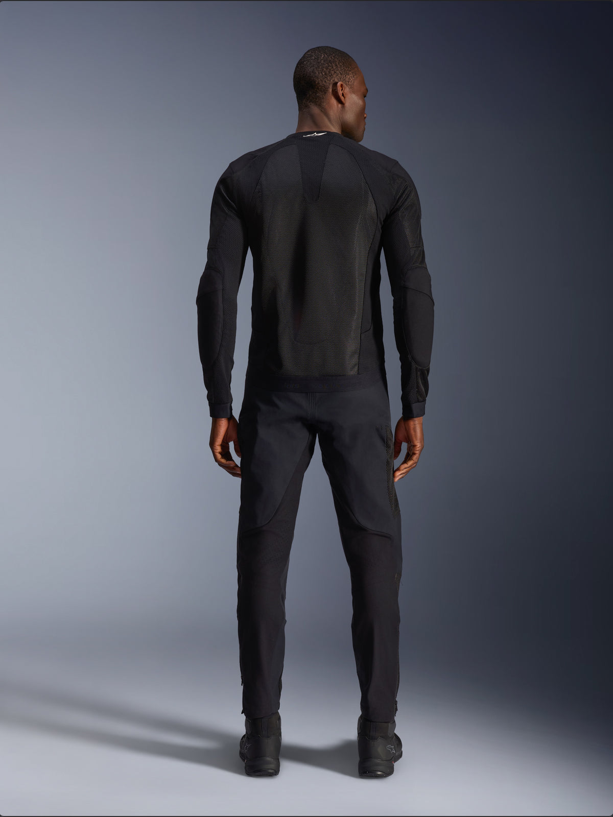 Alpinestars Troop-Air Jacke, technische Mesh-Motorradjacke für Herren, Schwarz, Rückansicht mit 2D-Tech-Mesh-Struktur und belüfteter Konstruktion, kombiniert mit schwarzer Motorradhose und Stiefeln.