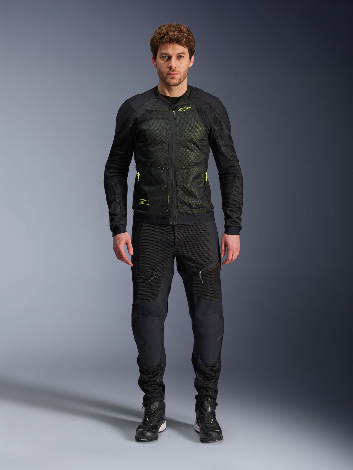 Male model wearing Alpinestars Troop-Air Jacket in Black Yellow Fluo, featuring technical mesh panels and bright yellow accents, paired with black riding pants and shoes, contemporary motorcycle apparel for warm weather