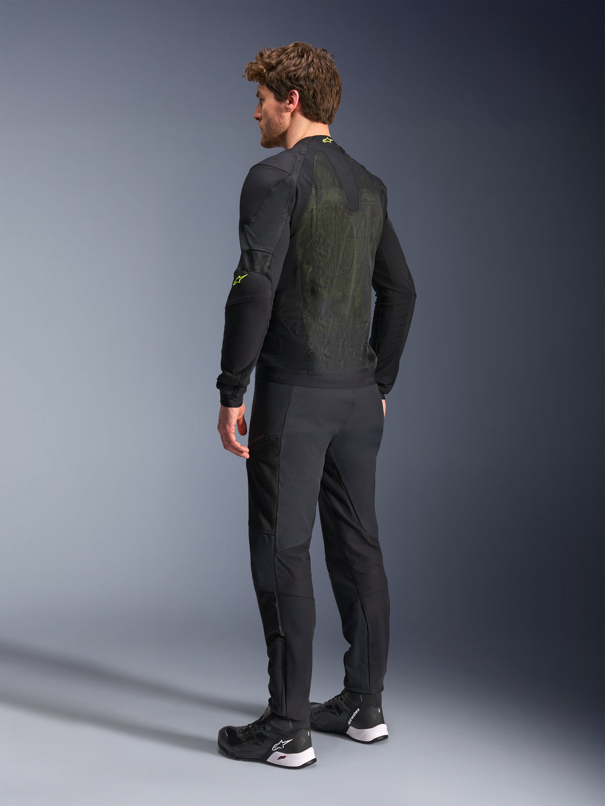 Alpinestars Troop-Air Jacket in Black and Yellow Fluo, rear view of a male model wearing the technical air jacket, featuring a large mesh back panel with yellow highlights and fluo yellow Alpinestars logos, paired with black motorcycle pants.