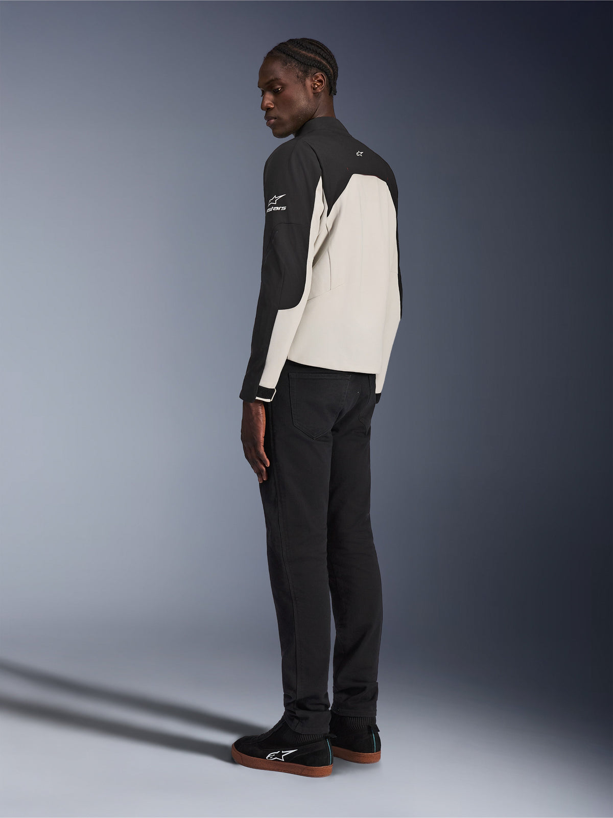 Alpinestars Provoke Jacke, urbane Motorradjacke, Schwarz und Metal Gray, Dreiviertel-Rückansicht an einem Model, zweifarbige Textilkonstruktion mit Alpinestars-Logo auf der Schulter, getragen mit schwarzer Hose und schwarzen Sneakern, zeitgemäßer Schutz für die Straße