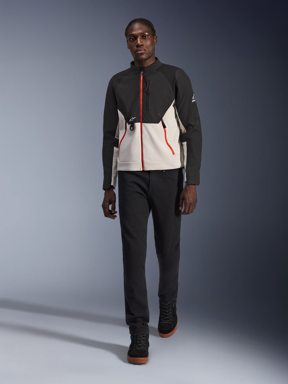 Männliches Model in der Alpinestars Provoke Jacke, urbane Motorradjacke in Schwarz und Metal Gray mit roten Reißverschluss-Akzenten, kombiniert mit schwarzer Hose und schwarzen High-Top-Schuhen, moderne Schutzausrüstung für Fahrten in der Stadt