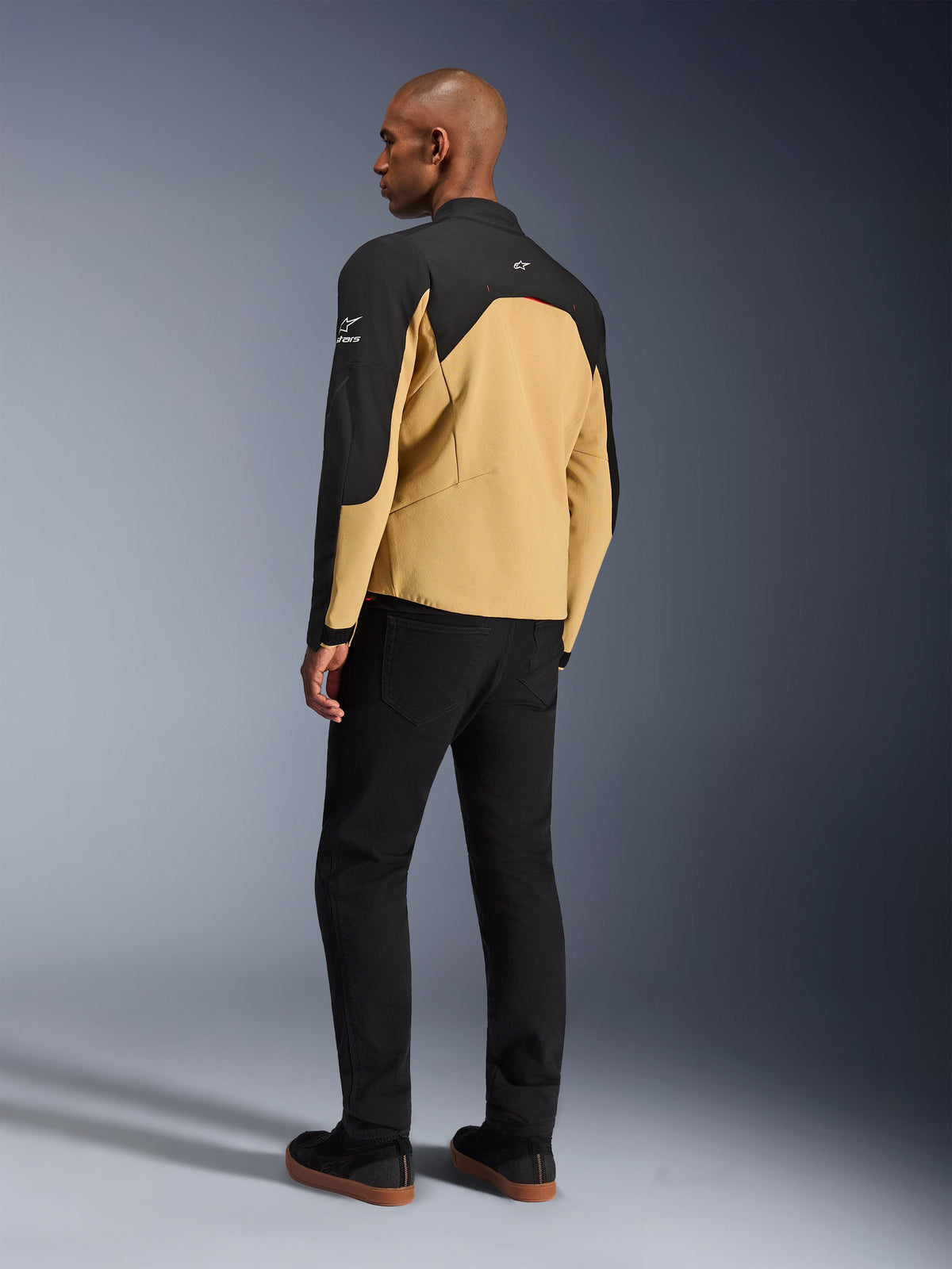 Alpinestars Provoke Jacket, urban motorcycle jacket in Black Camel, rear three-quarter view, camel-colored body with black shoulder and sleeve panels, white Alpinestars logos, worn with black pants, contemporary technical riding gear